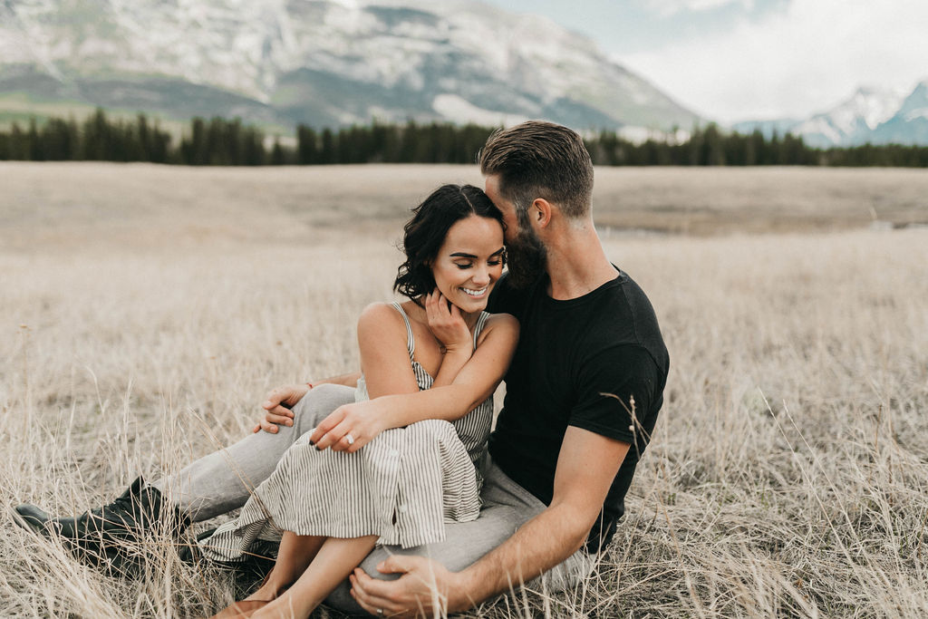 Couple sitting and cuddling during their engagement Session in the mountains captured by Kadie Hummel Photography.
