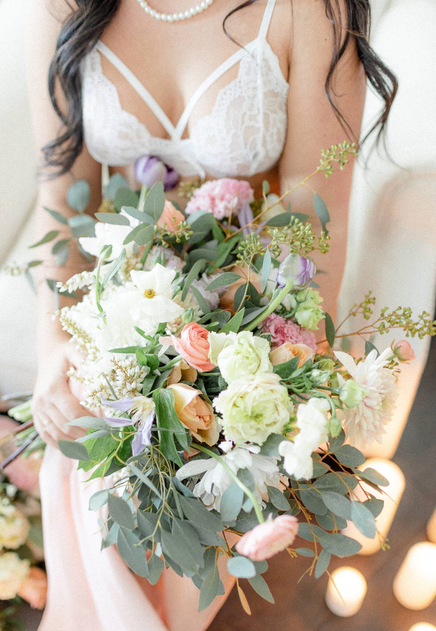 Feminine bridal boudoir, bride-to-be wearing romantic white lace lingerie and pearls holding spring inspired wedding florals 
