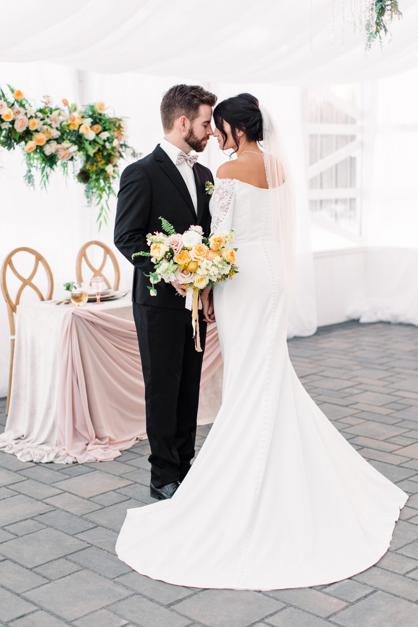 Bride and groom standing in an embrace at stunning tented wedding at Sunflower & Swallow. Spring inspired reception decor, complete with yellow and peach floral installation. 