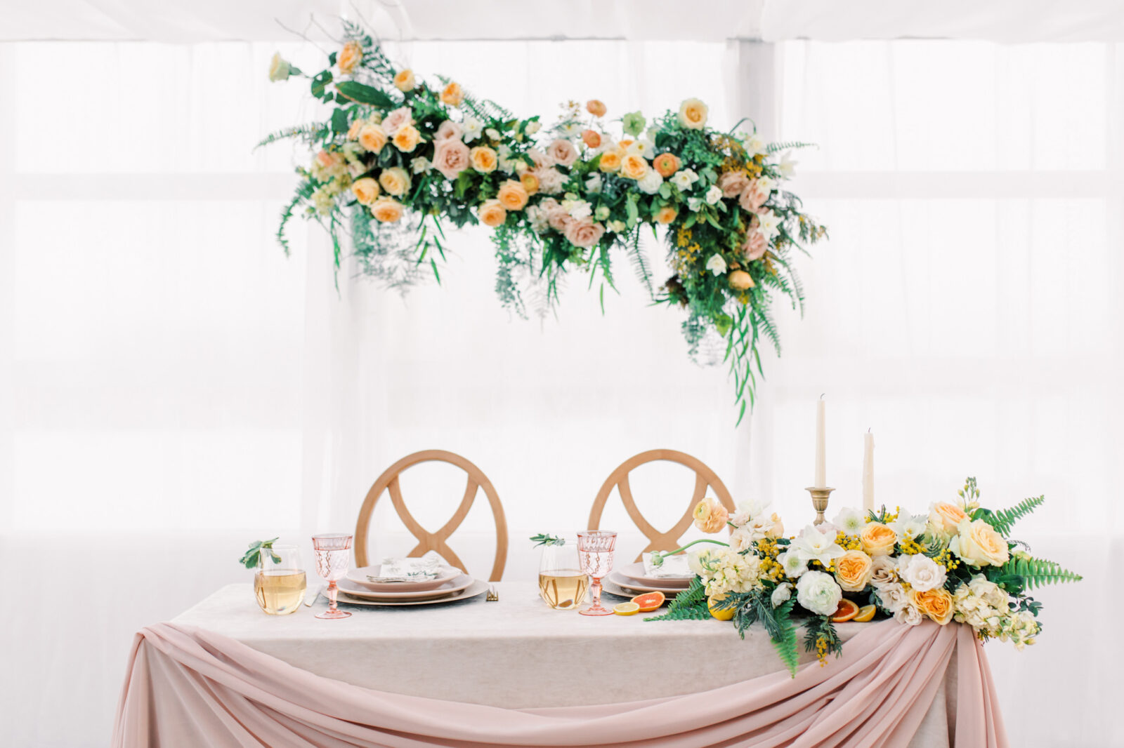 Sweetheart table design with yellow and peach spring inspired floral arrangements, custom pink glassware, plates, and stemware, designed by Changing Dreams to Reality