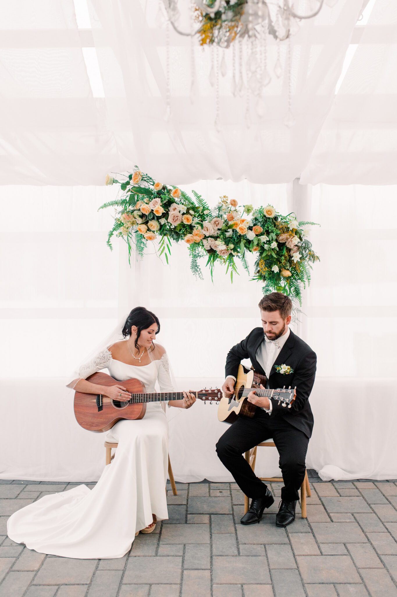 Fun bride and groom playing guitar at summer tented wedding reception in Sunflower & Swallow's elegant, modern greenhouse located in Bezanson, Alberta