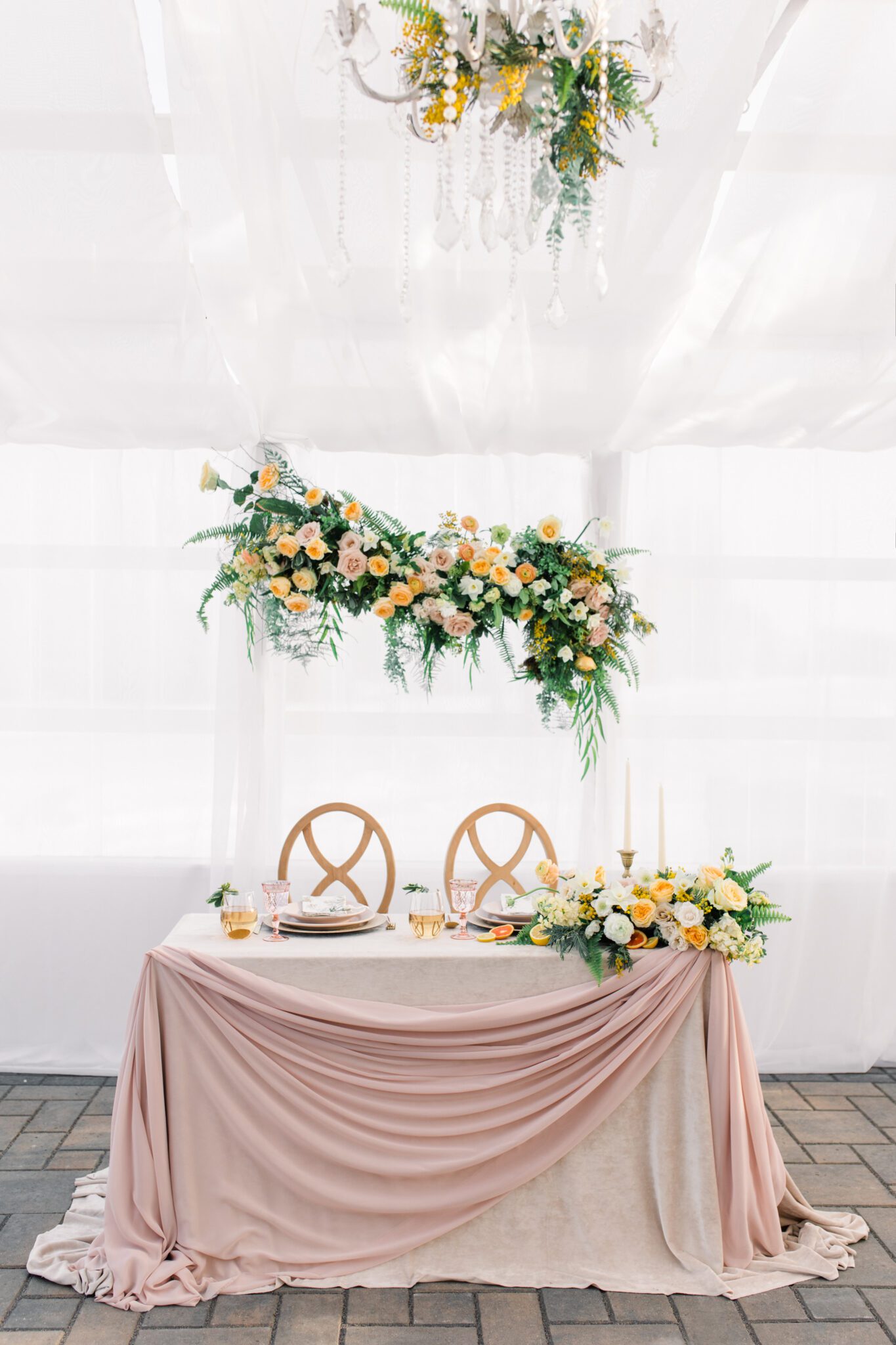 Sweetheart table design with yellow and peach spring inspired floral arrangements, custom pink glasswear, plates, and stemware, captured by Kayla Lynn Photography
