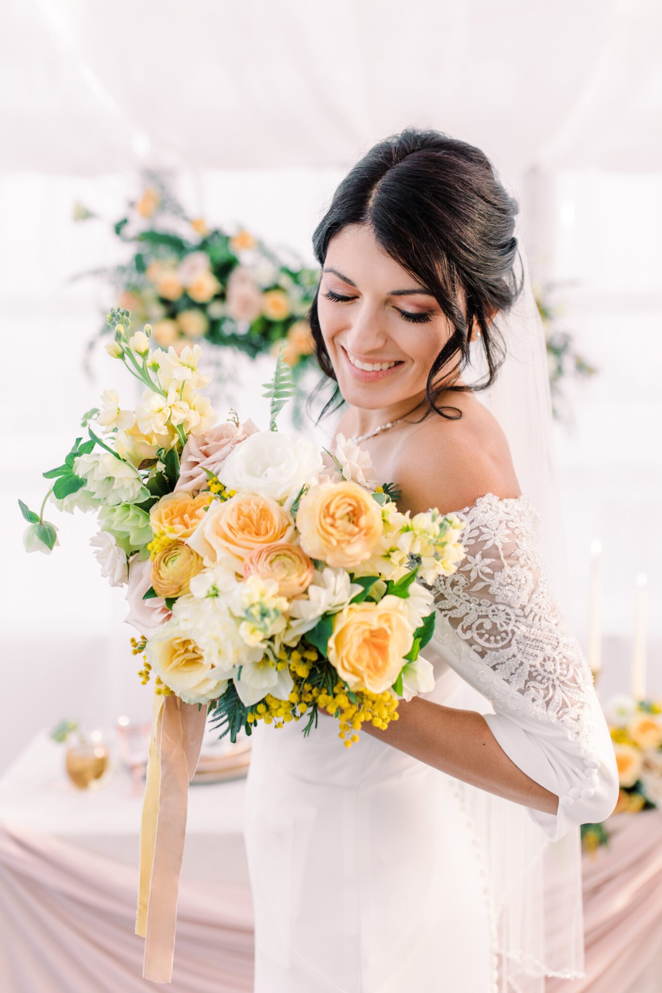 Bride holding yellow and peach bridal bouquet designed by Little Petal Company, wearing off-the-shoulder wedding gown with lace sleeve detail, hair and makeup by Desire at The Headroom