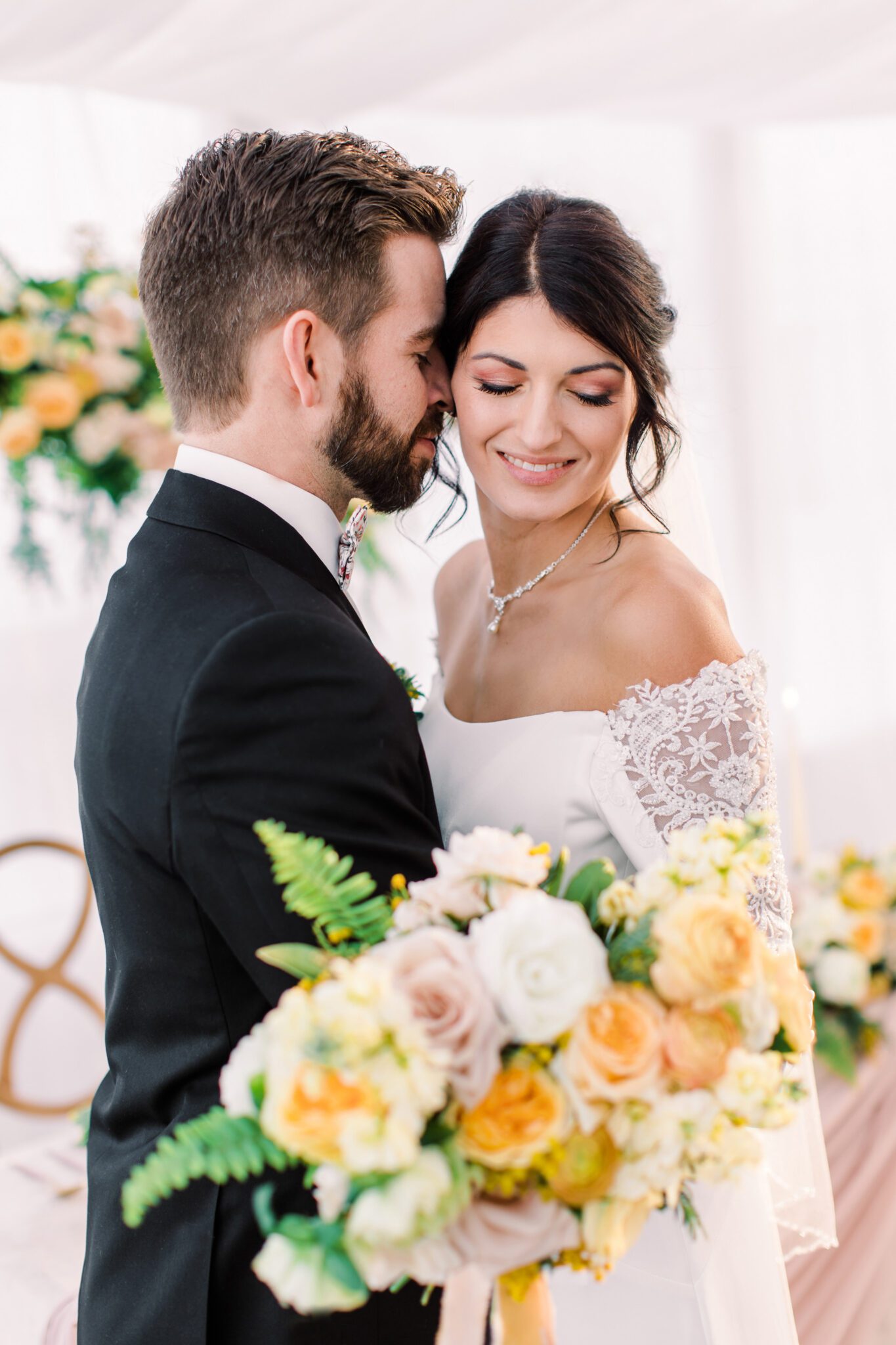 Bride and groom embracing at stunning tented wedding at Sunflower & Swallow, bride holding yellow and peach bridal bouquet, summer wedding inspiration