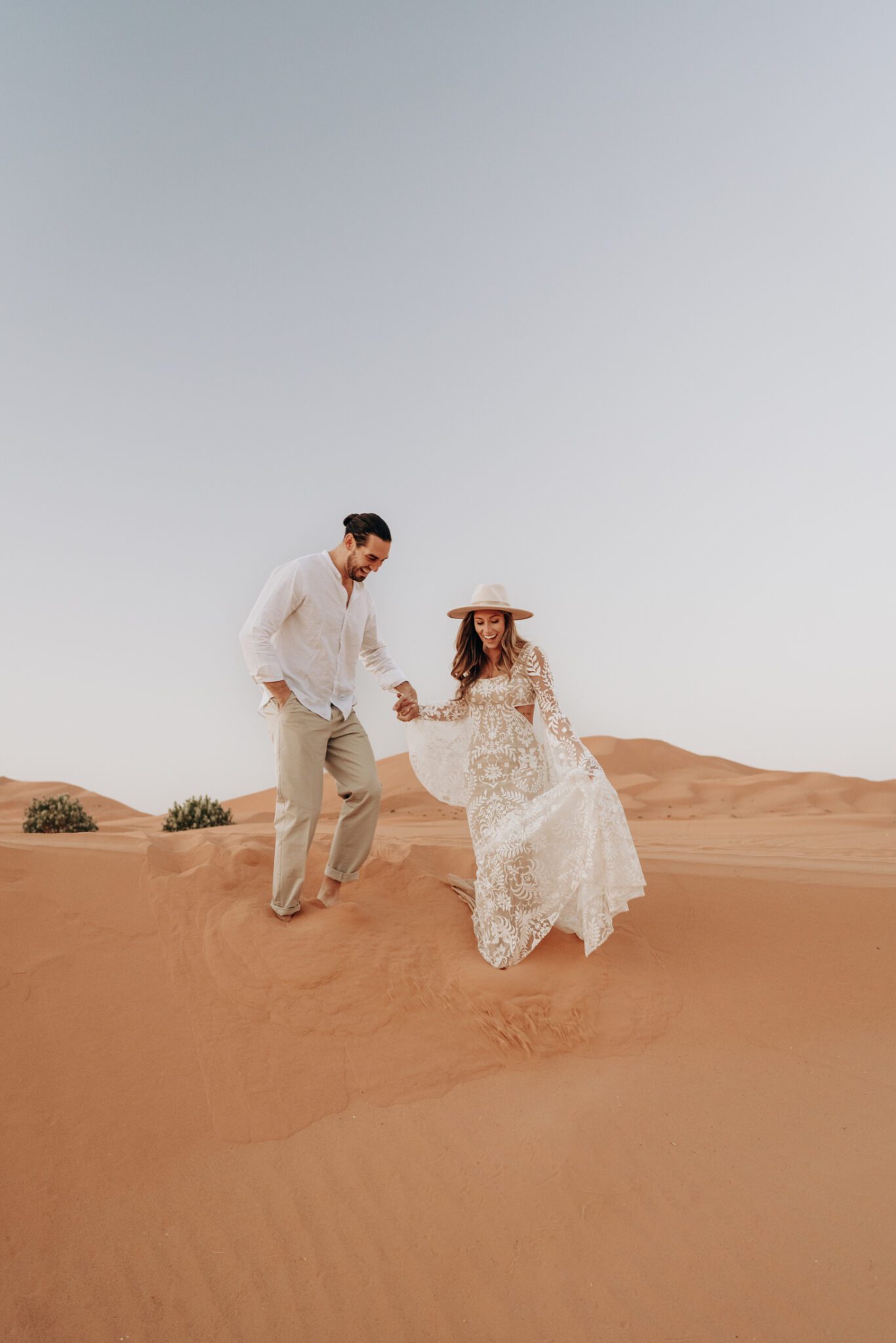 Couple holding hands walking through the sand, during their boho sunrise engagement session.