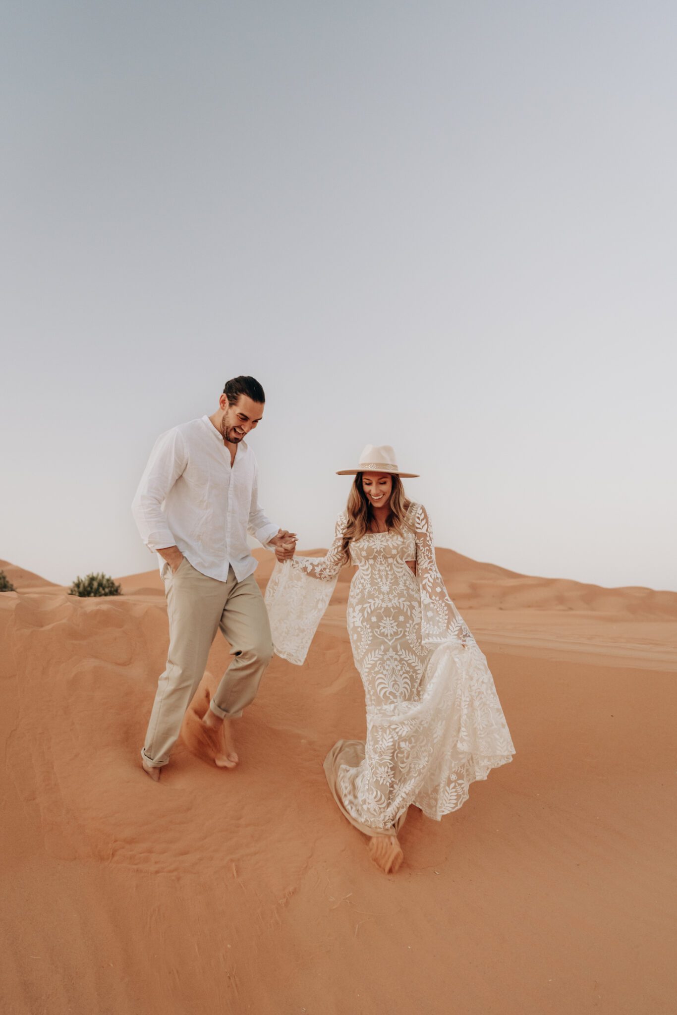 Couple holding hands walking through the sand, during their boho sunrise engagement session.