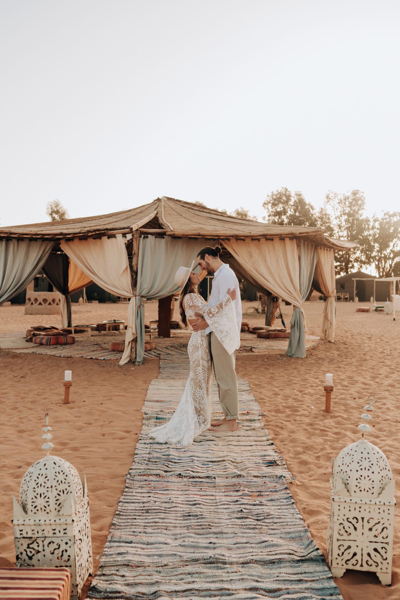 Couple embracing in front of tent at their Moroccan desert camp engagement. 