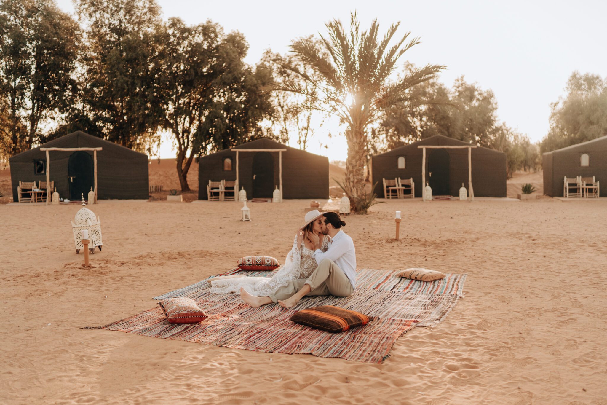 Couple sitting on colourful jute rug in front of tents at the Madu Luxury Camp in the Sahara Desert.