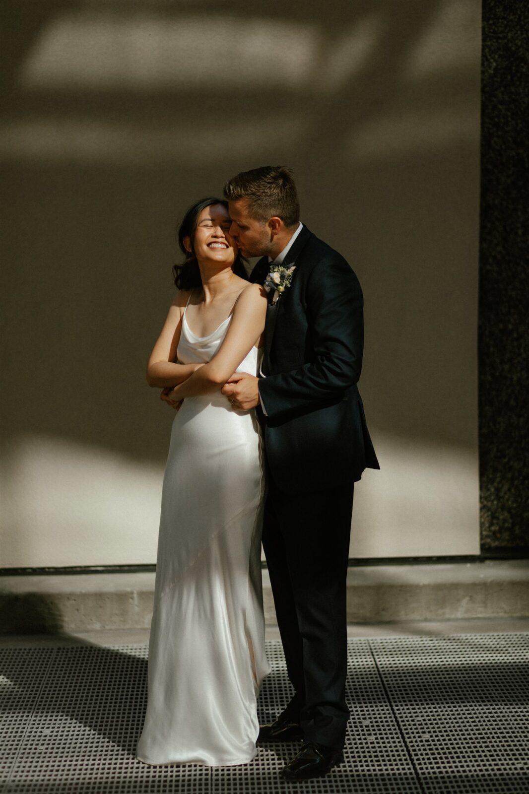Couple embracing during intimate Vancouver wedding. Bride wearing sleek satin bridal gown from Park and Fifth.