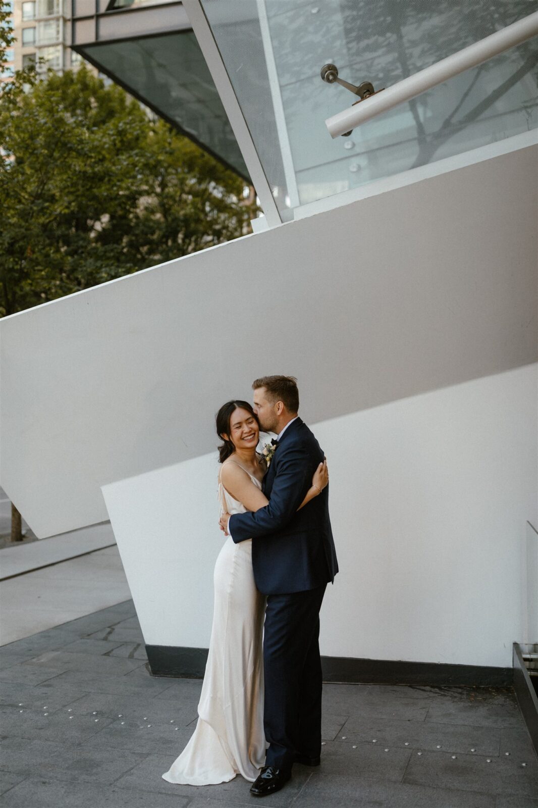 Couple embracing during intimate Vancouver wedding. Sleek satin bridal gown from Park and Fifth.