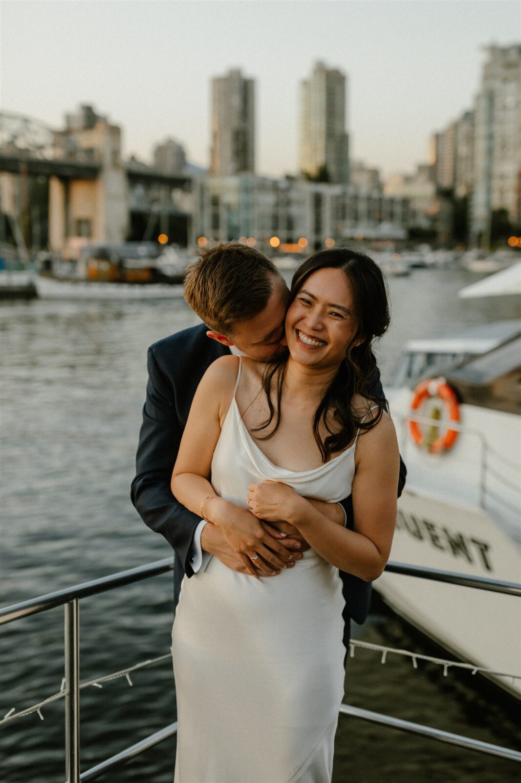 Bride and groom embrace on boat during Vancouver's Festival of Lights. Bridal hair by The Attic Hair Studio, and makeup by Beauty Awakened.