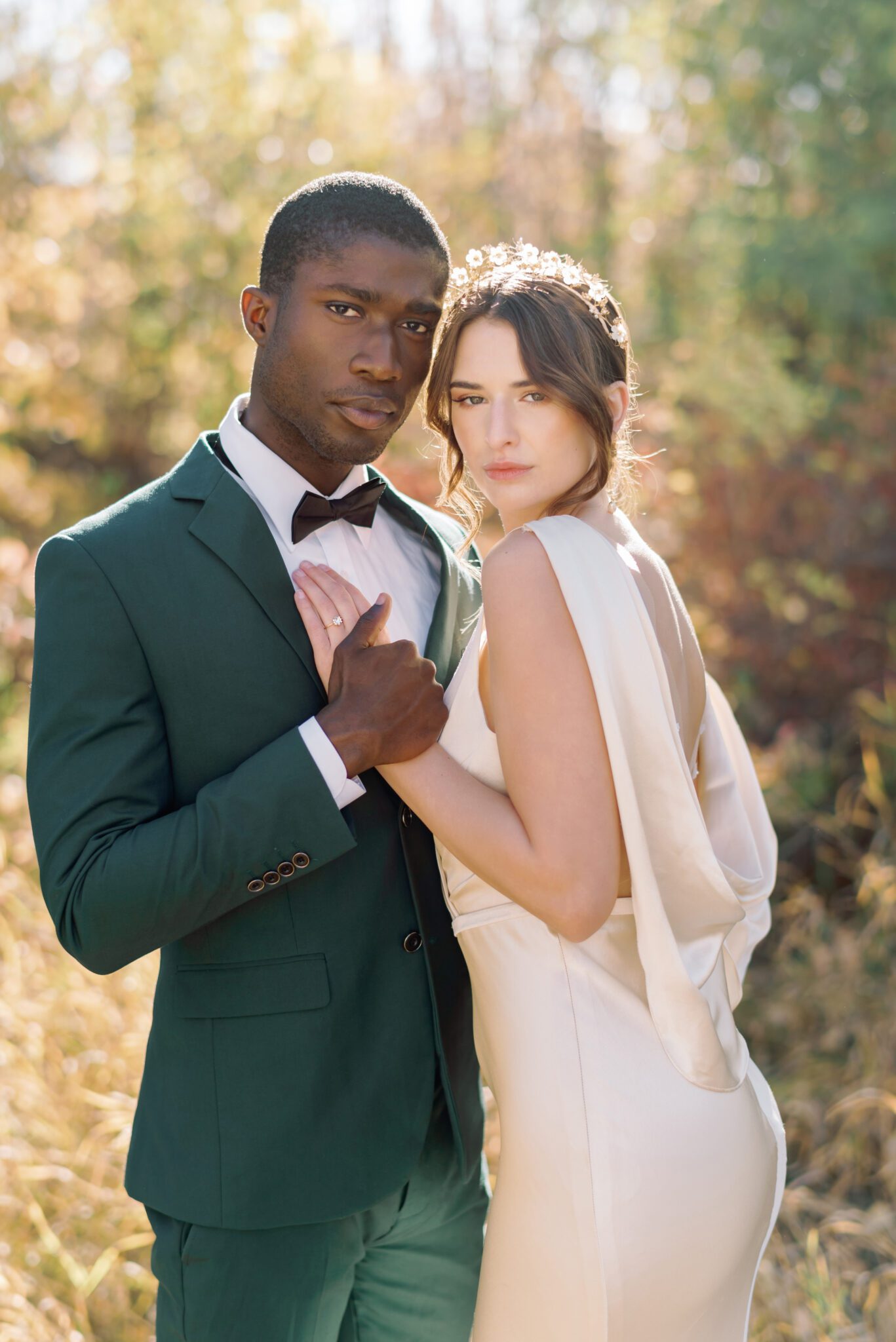 Couple embracing at intimate Fall wedding, groom wearing emerald green suit, and bride in elegant satin gown with low back.