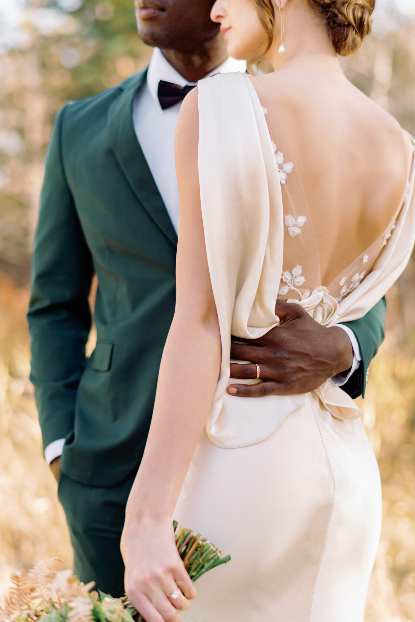 Couple embracing at intimate Fall wedding, groom wearing emerald green suit, and bride in elegant satin gown. 