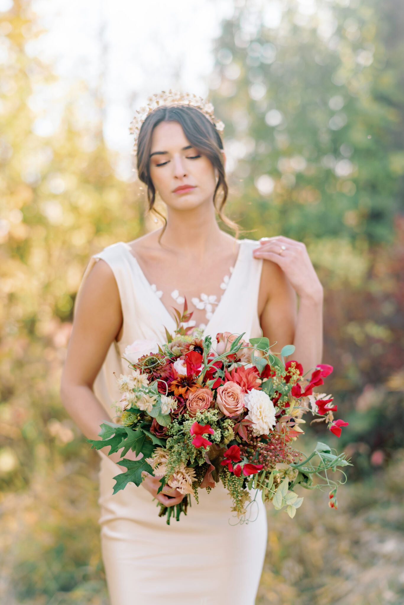 Bride wearing elegant champagne-toned satin wedding gown holding organic fall floral arrangements by Petal and Stem.