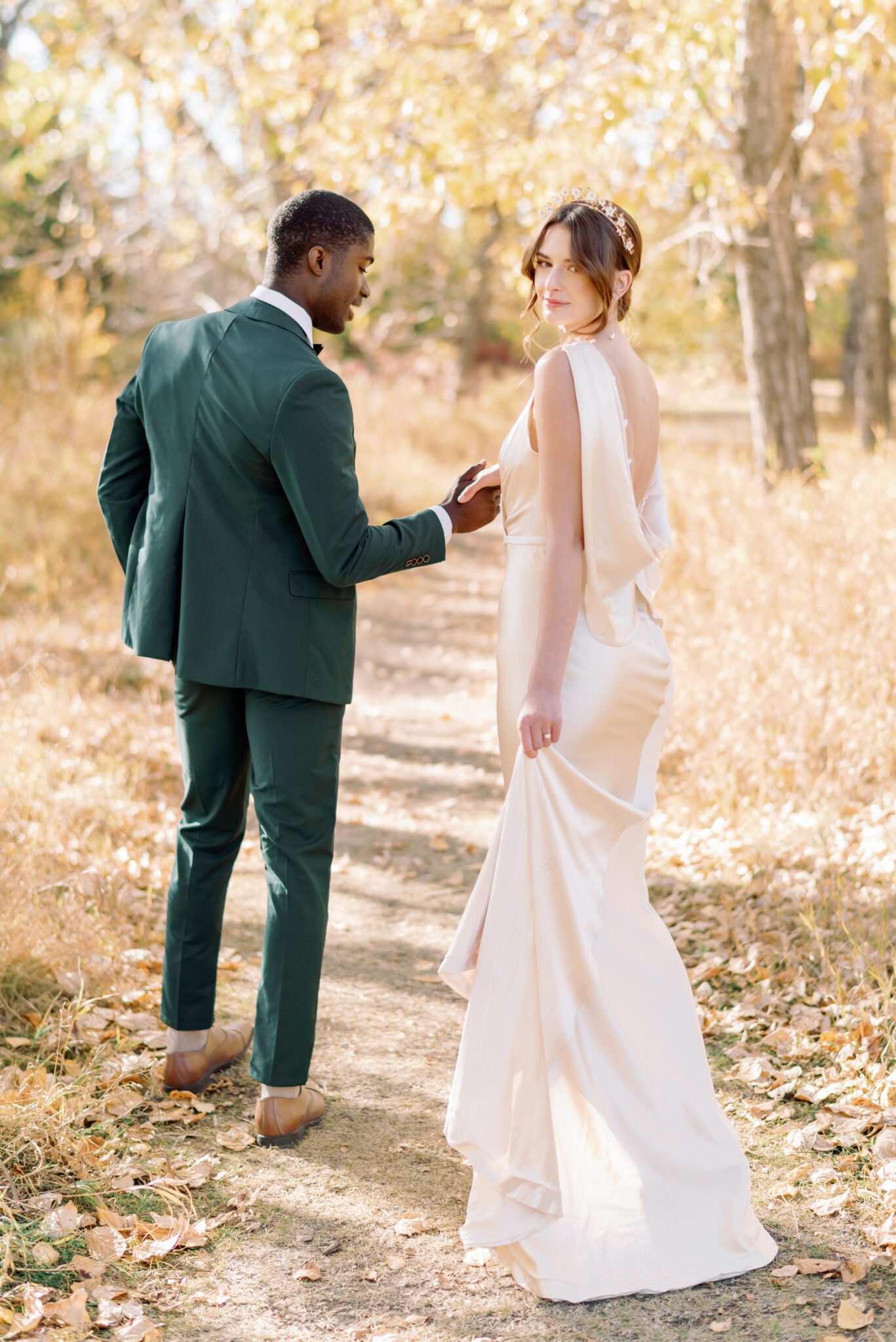 Couple walking at intimate Autumn wedding, groom wearing emerald green suit, and bride in elegant satin gown. 