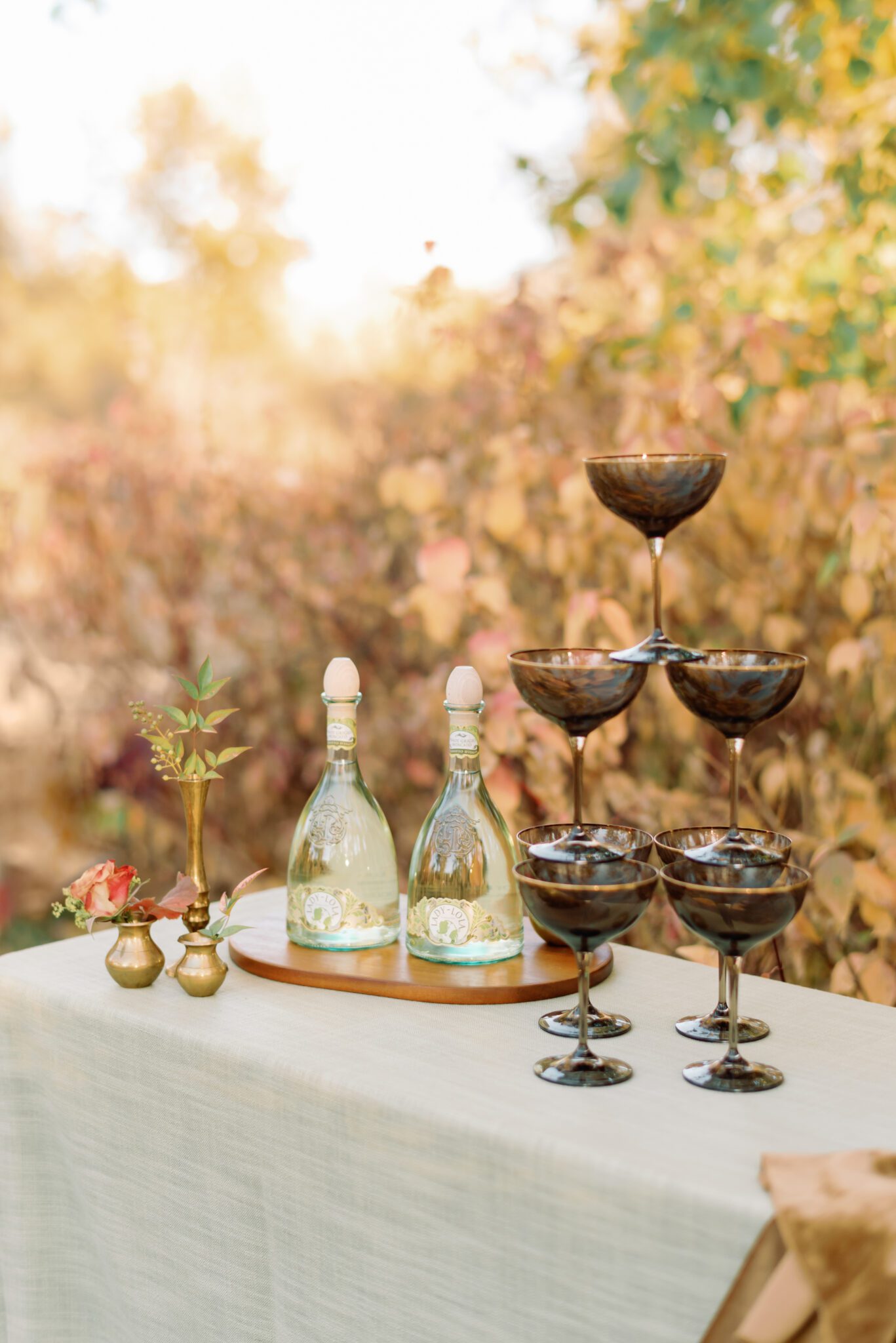 Outdoor champagne table featuring champagne tower with smoke-tinted glassware from Modern Rentals and champagne bottles with uniquely elegant green-tinted glass. 