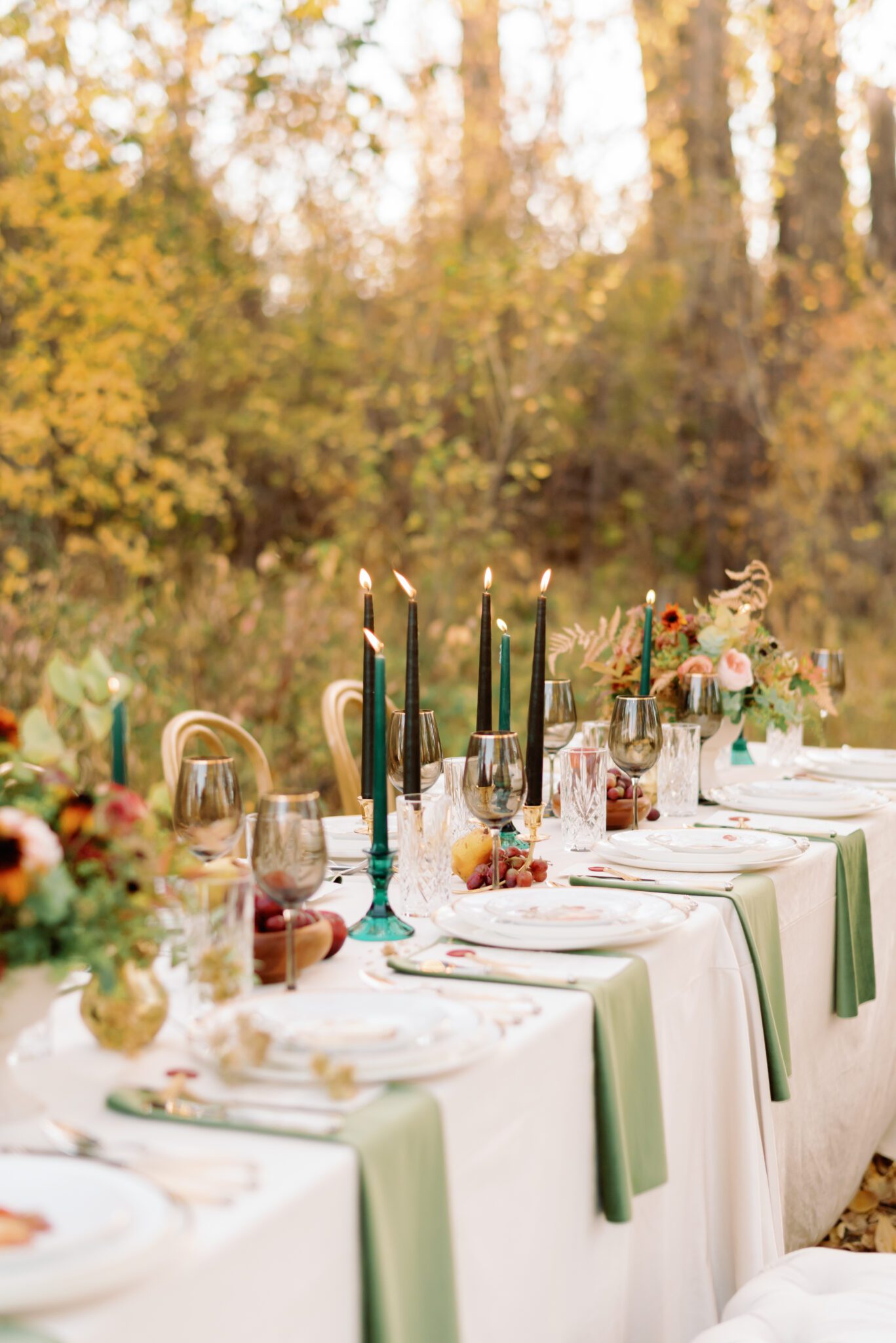 Al fresco dining at golden hour. Intimate autumn wedding reception tablescape featuring olive green, burgundy and rust details, elegant menus with crimson wax seals and gold tassel accents, as well as smoke tinted glassware, gold-rimmed vintage china with fruit still lifes painted on them, pearl cutlery, and antique gold pear candleholders