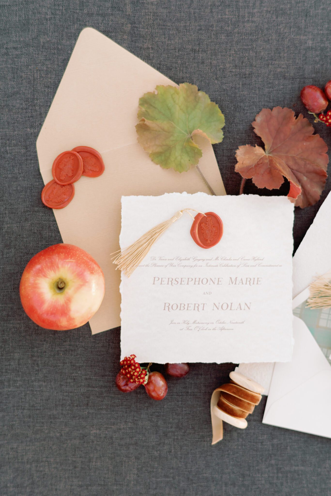 Wedding invitation flatlay with fall wedding stationery featuring handmade paper with a hand deckled edge and crimson wax seals with gold tassel accents.