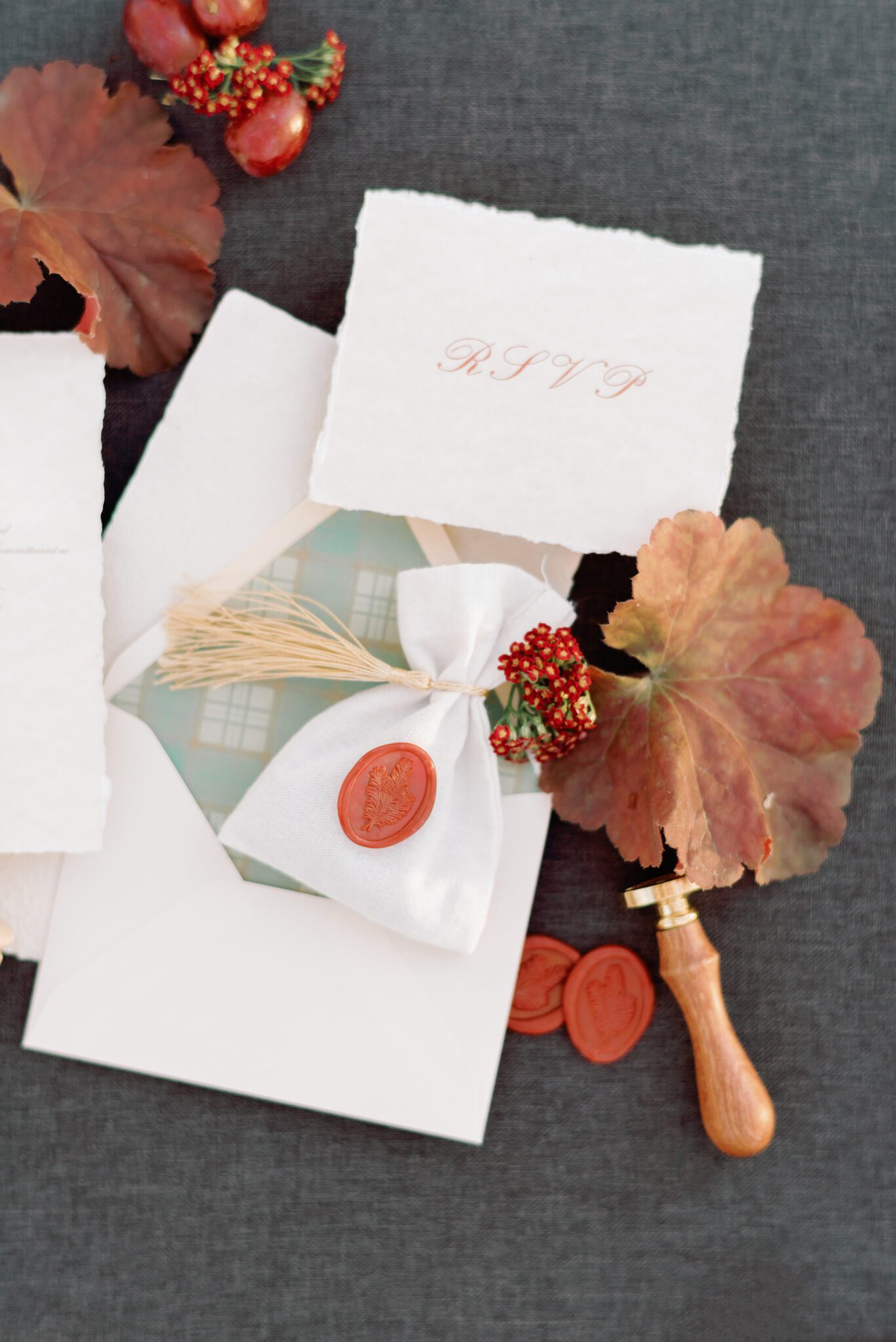 Wedding invitation flatlay with fall wedding stationery featuring handmade paper with a hand deckled edge and crimson wax seals with gold tassel accents.
