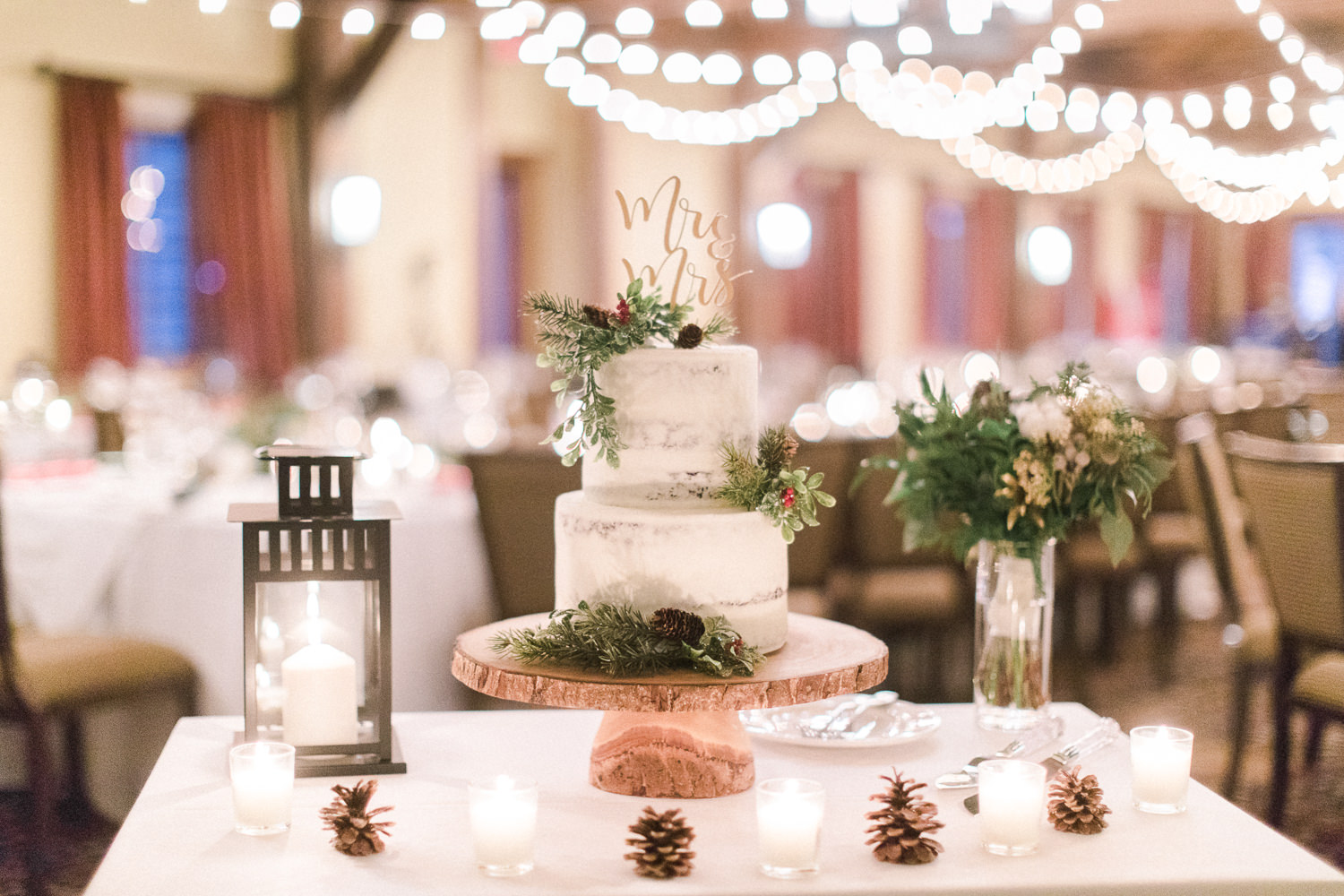 Elegant winter two-tiered cake with textured greenery and gold handwritten sign, winter wedding inspiration. 