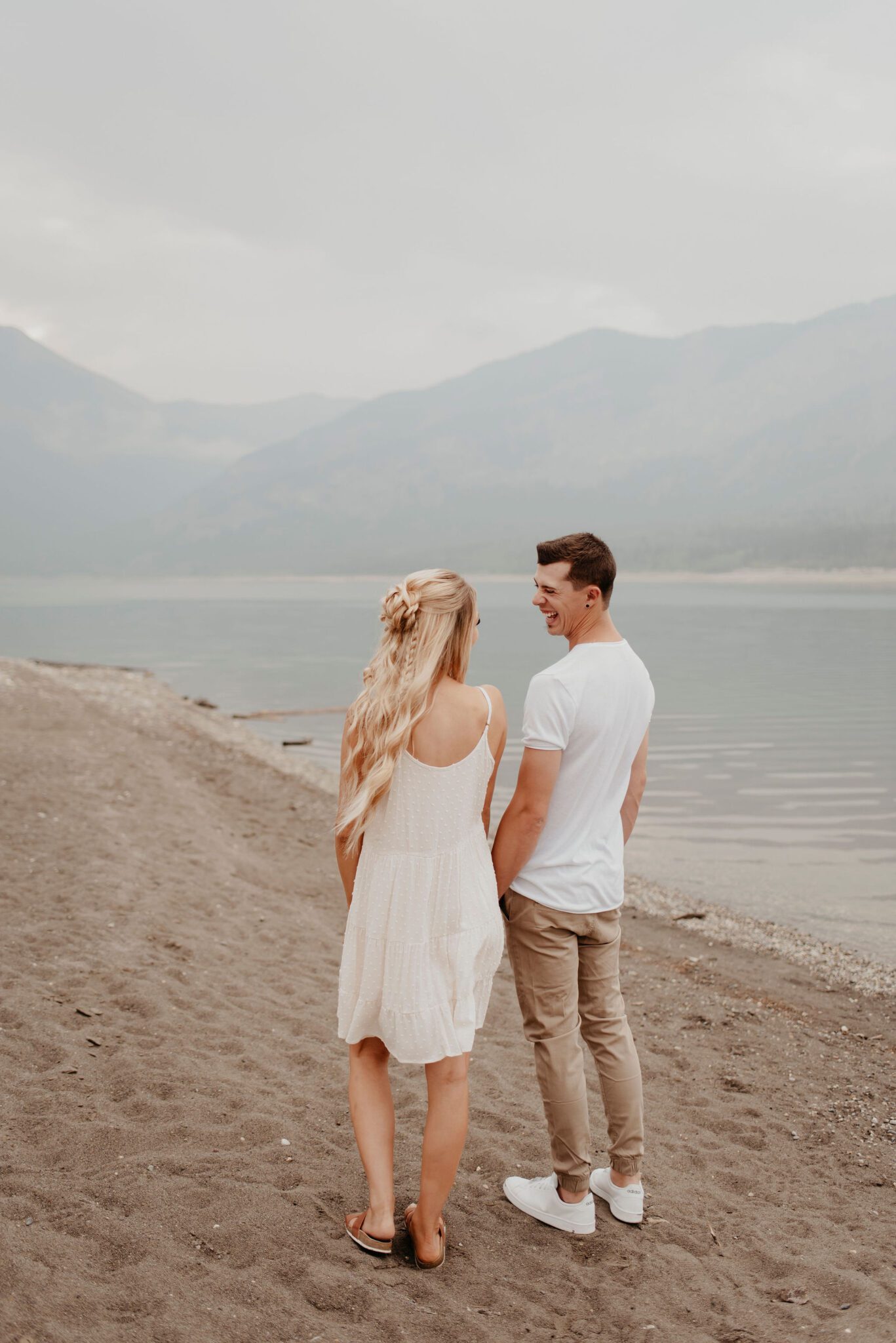 Young couple laughing together on the beach during this fun summer evening photoshoot in the mountains of Alberta.
