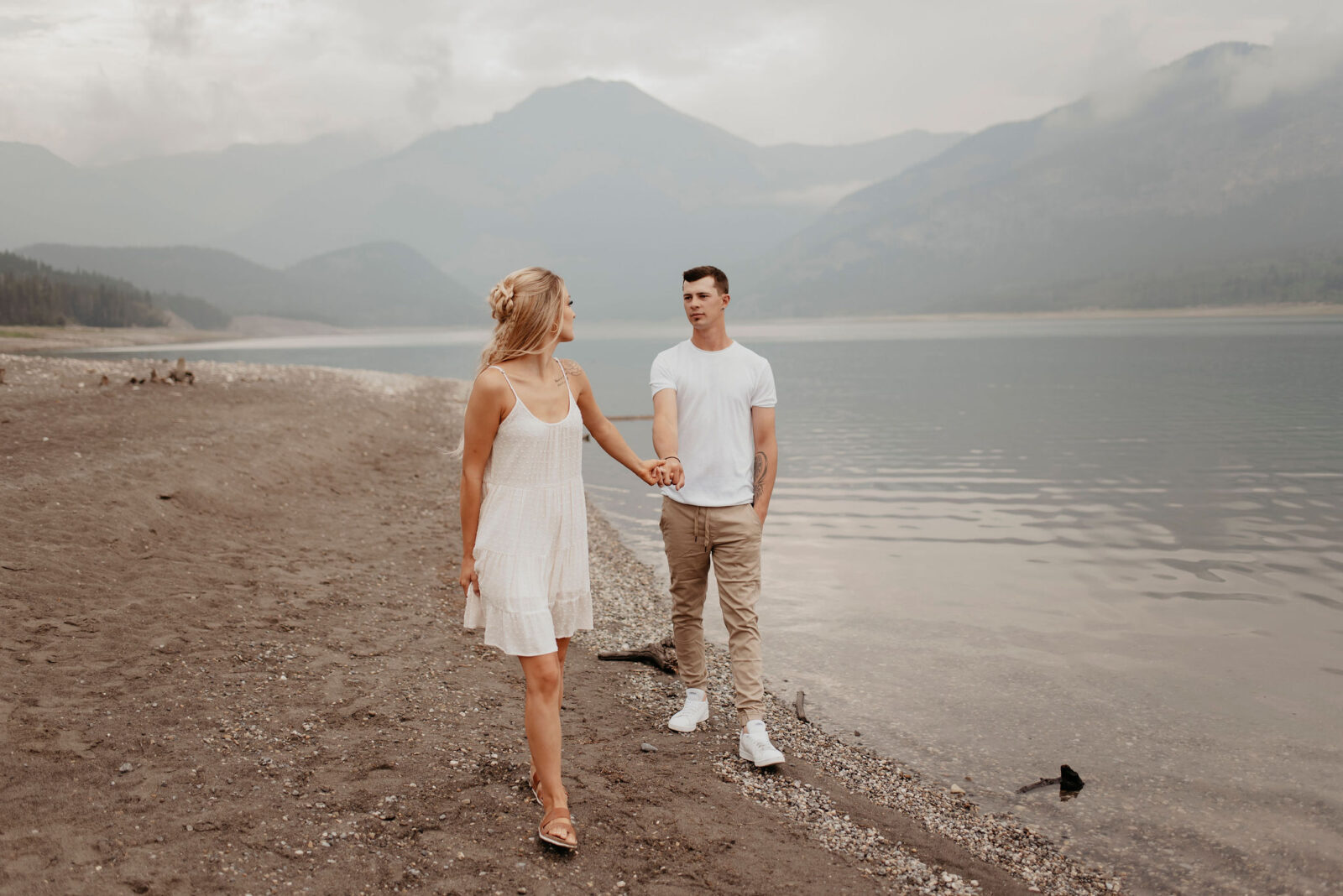Couple walking together on the beach at Barrier Lake. Alberta engagement photography by Kelsey Vera.