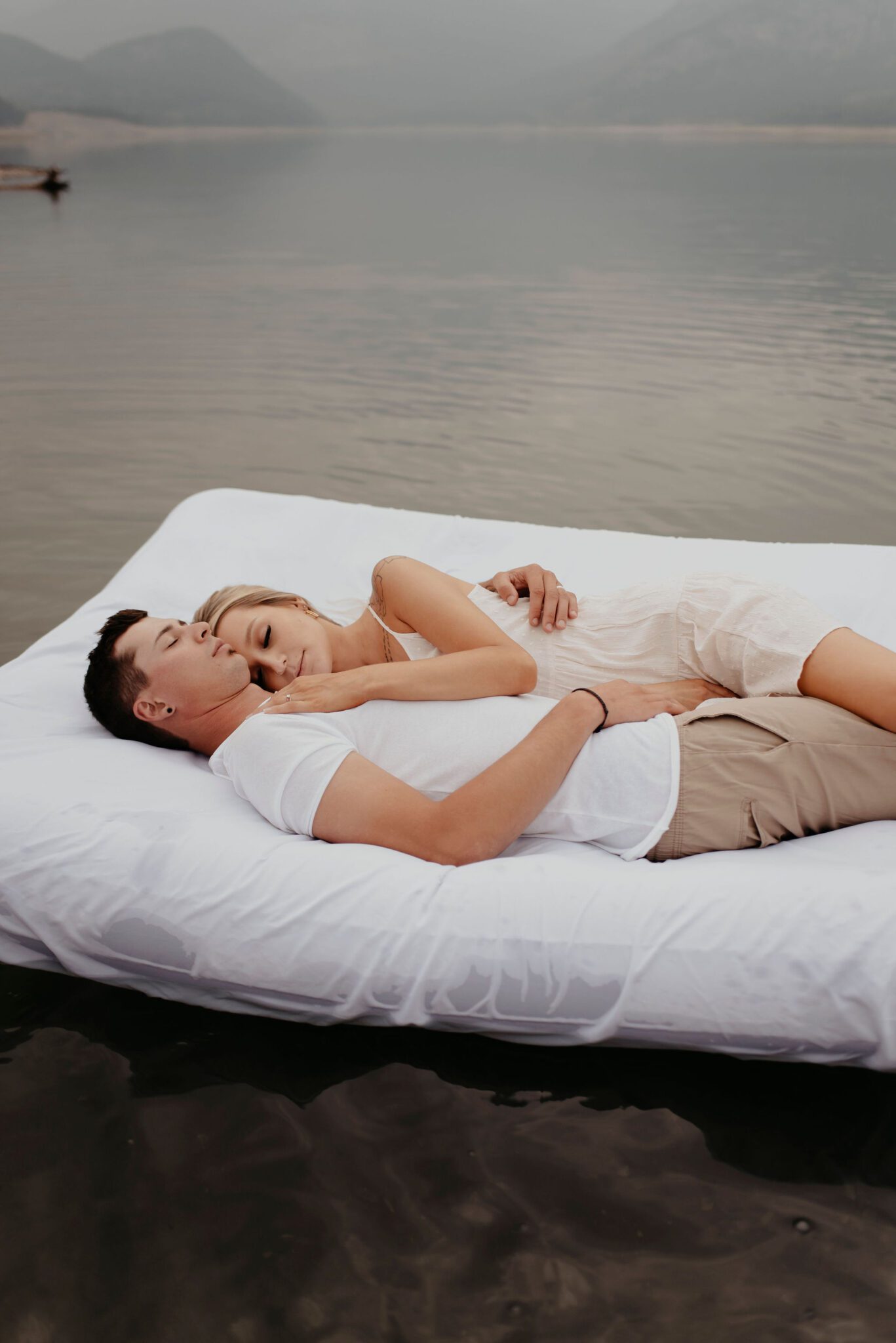 Couple snuggling together on floating mattress during their fun summer engagement session on Barrier Lake, Alberta. 