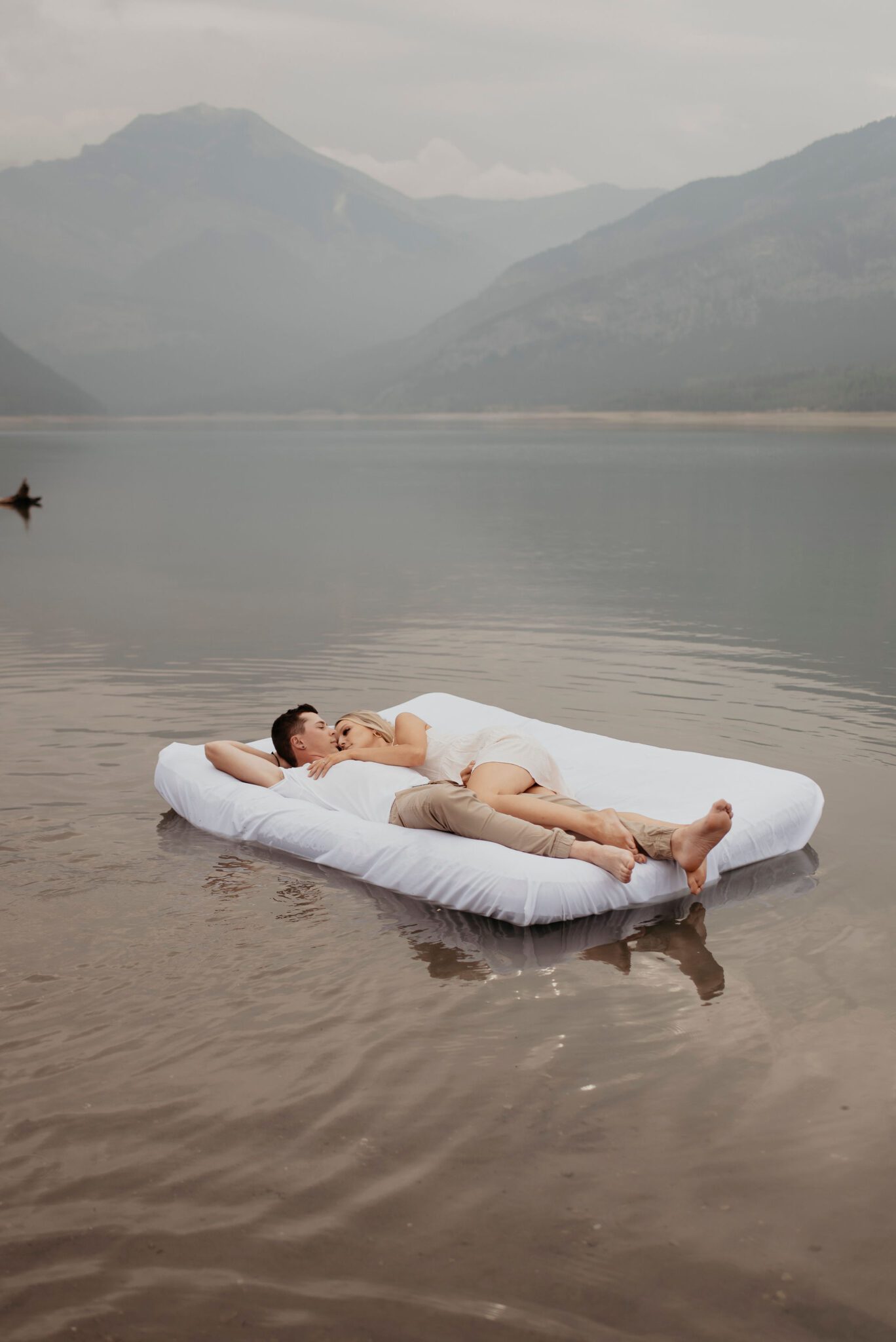 Couple snuggling together on floating mattress during their fun summer engagement session on Barrier Lake, Alberta. 