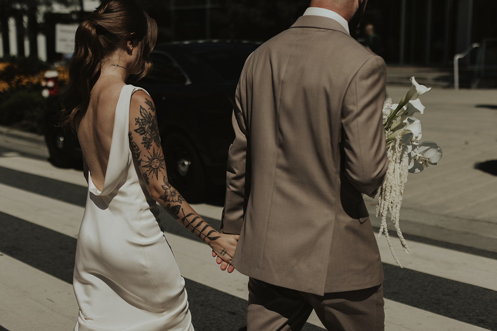 Couple walking holding hands in North Vancouver. Bride wearing sleek satin gown by Savannah Miller. Groom in earthy brown suit.