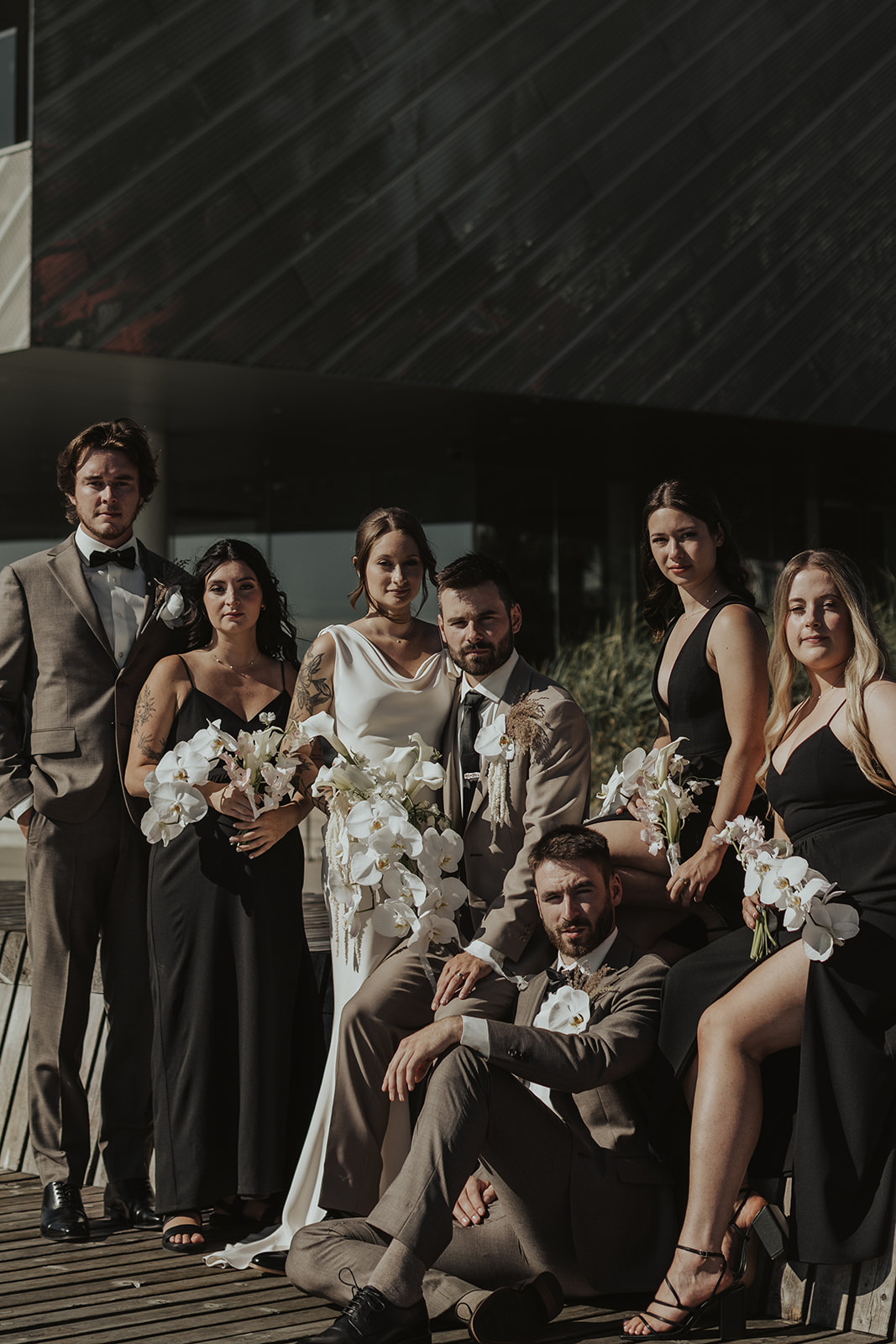 Moody bridal party portrait in downtown Vancouver, black bridesmaids dresses, earthy brown groomsmen suits, stunning white orchid bouquets by The Flower Library.