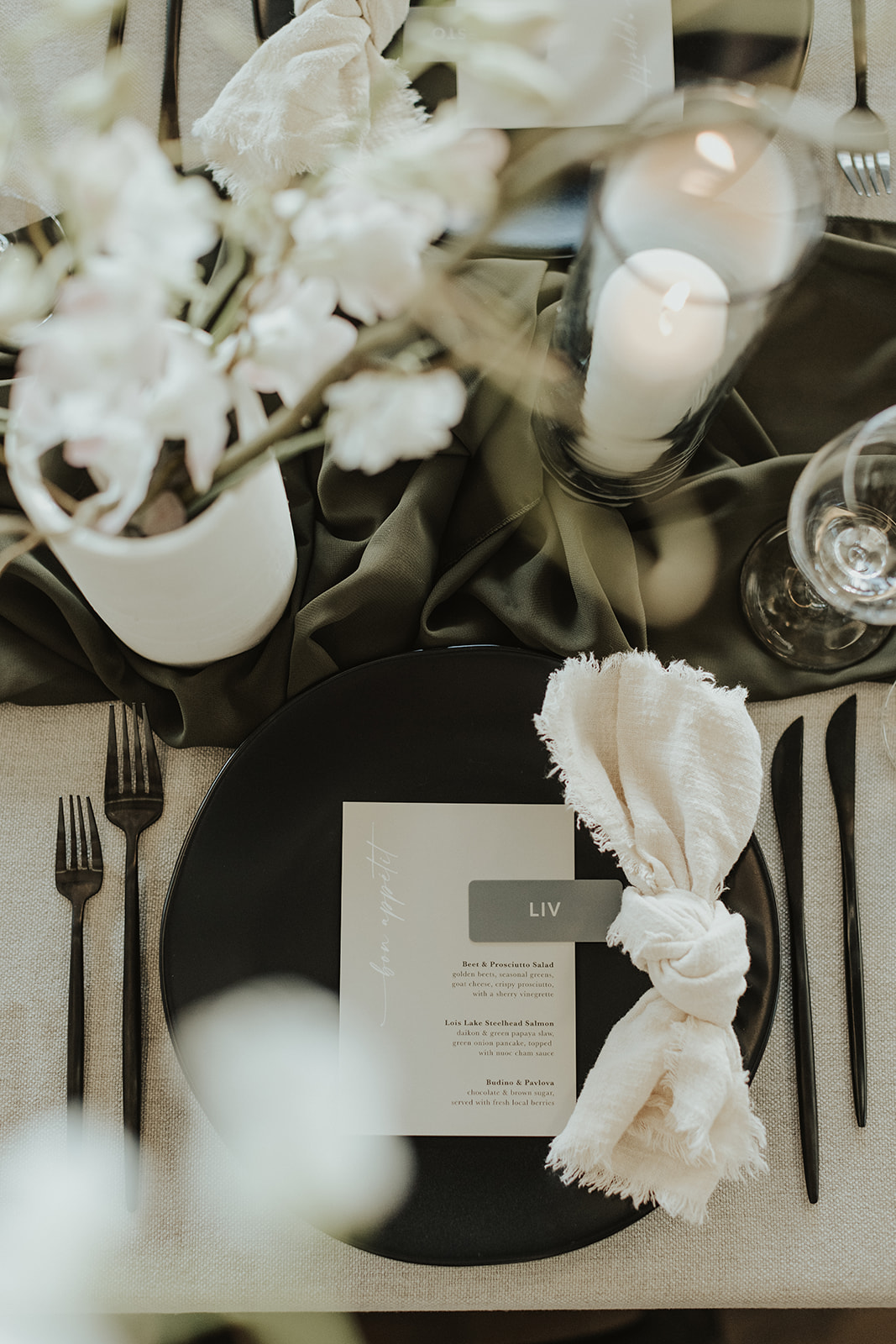 Black and white moody and minimalist wedding reception. Wedding table setting with modern black plate and black cutlery with knotted napkin.