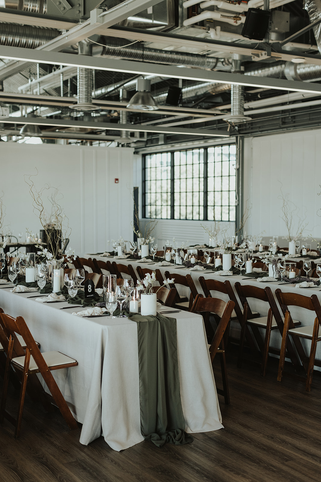 Moody wedding reception at industrial venue, The Wallace in North Vancouver. Decorated with olive green table runners, and earthy, organic florals by The Flower Library.