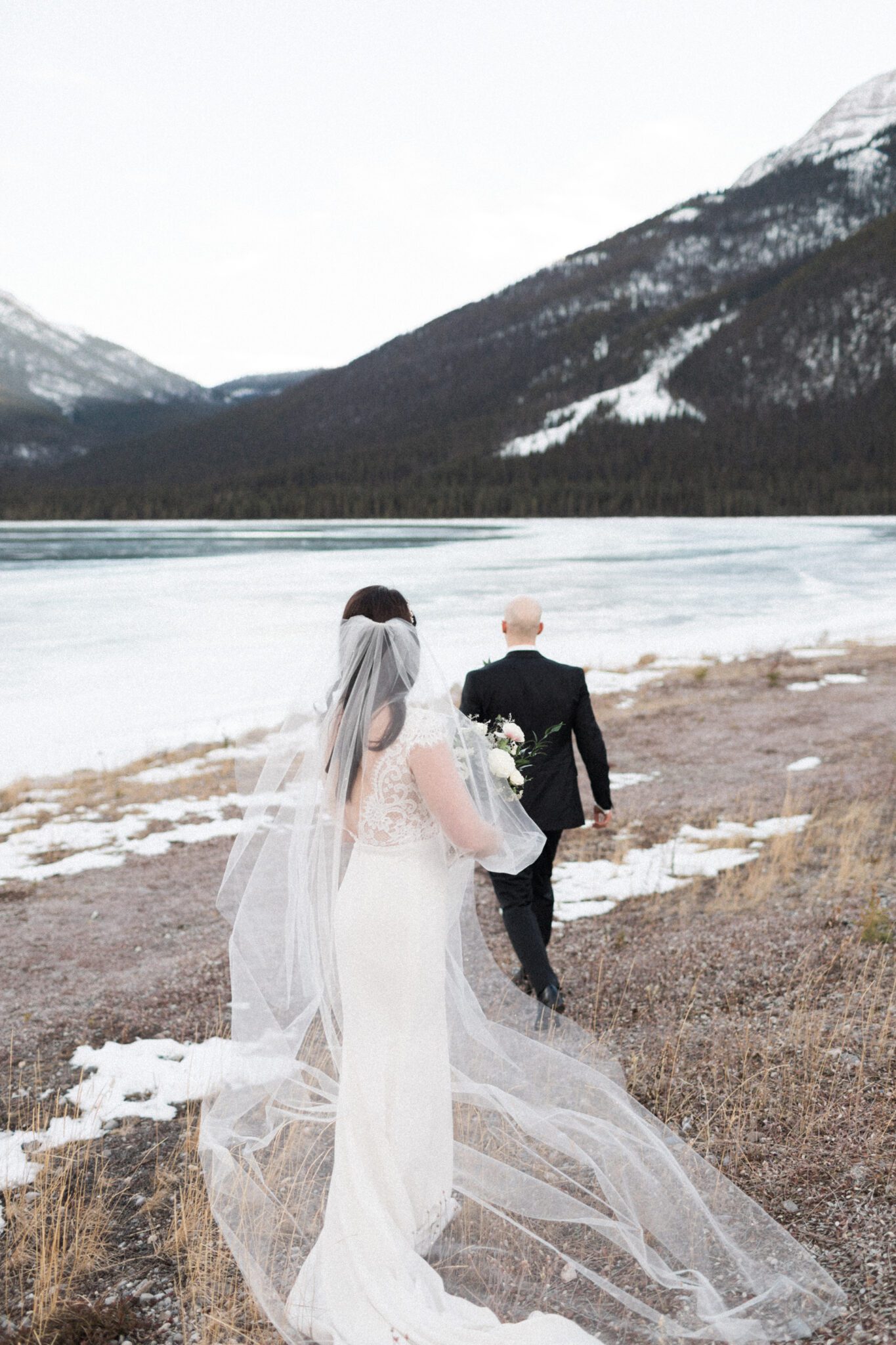 Couple walking down to the water with a stunning mountain backdrop and lake view, winter wedding inspiration. 