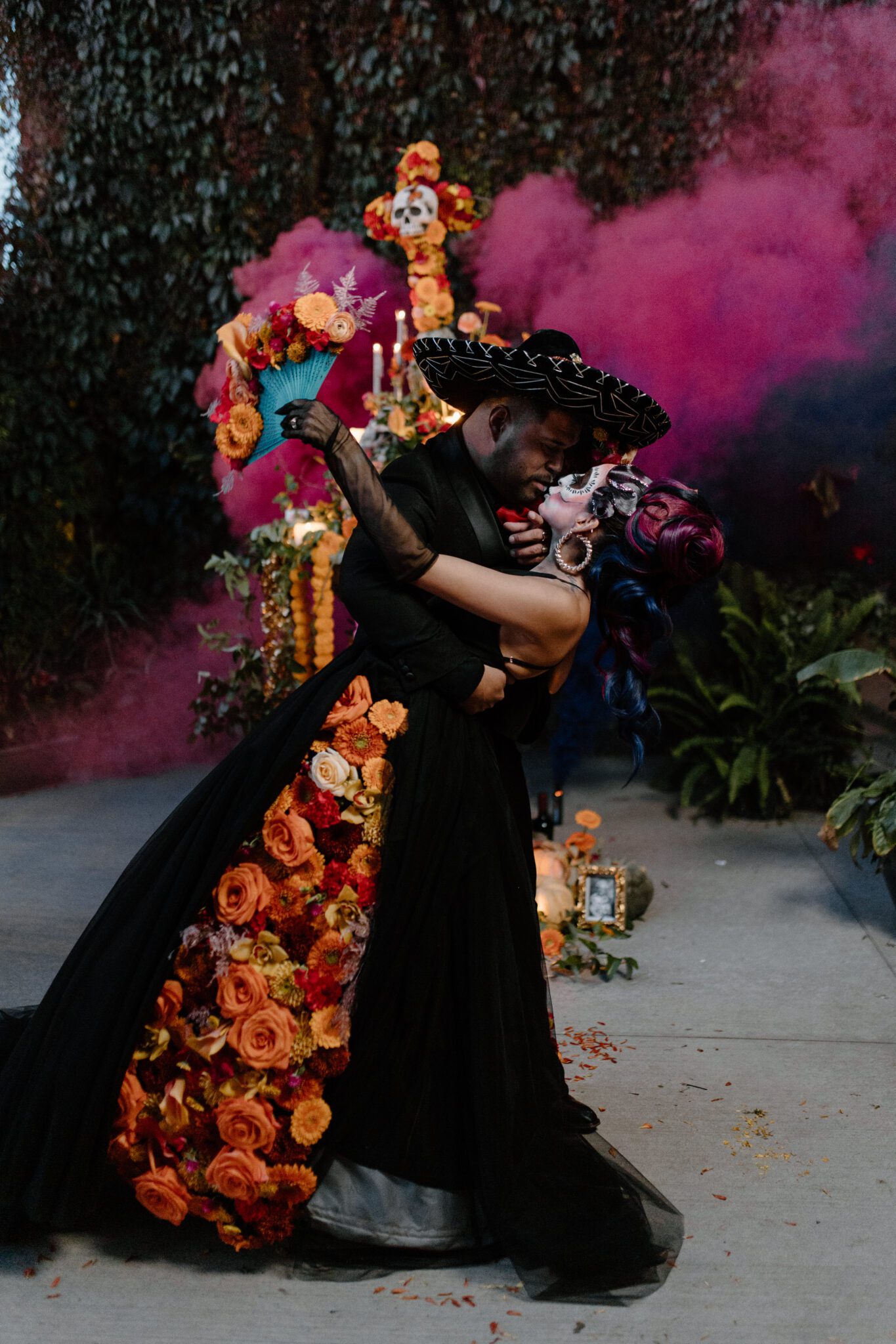 Couple embracing for Day of the Dead inspiration photo, captured by Nikki Collette. Black and pink smoke bombs, and fiery fall florals by Calyx Floral Design.