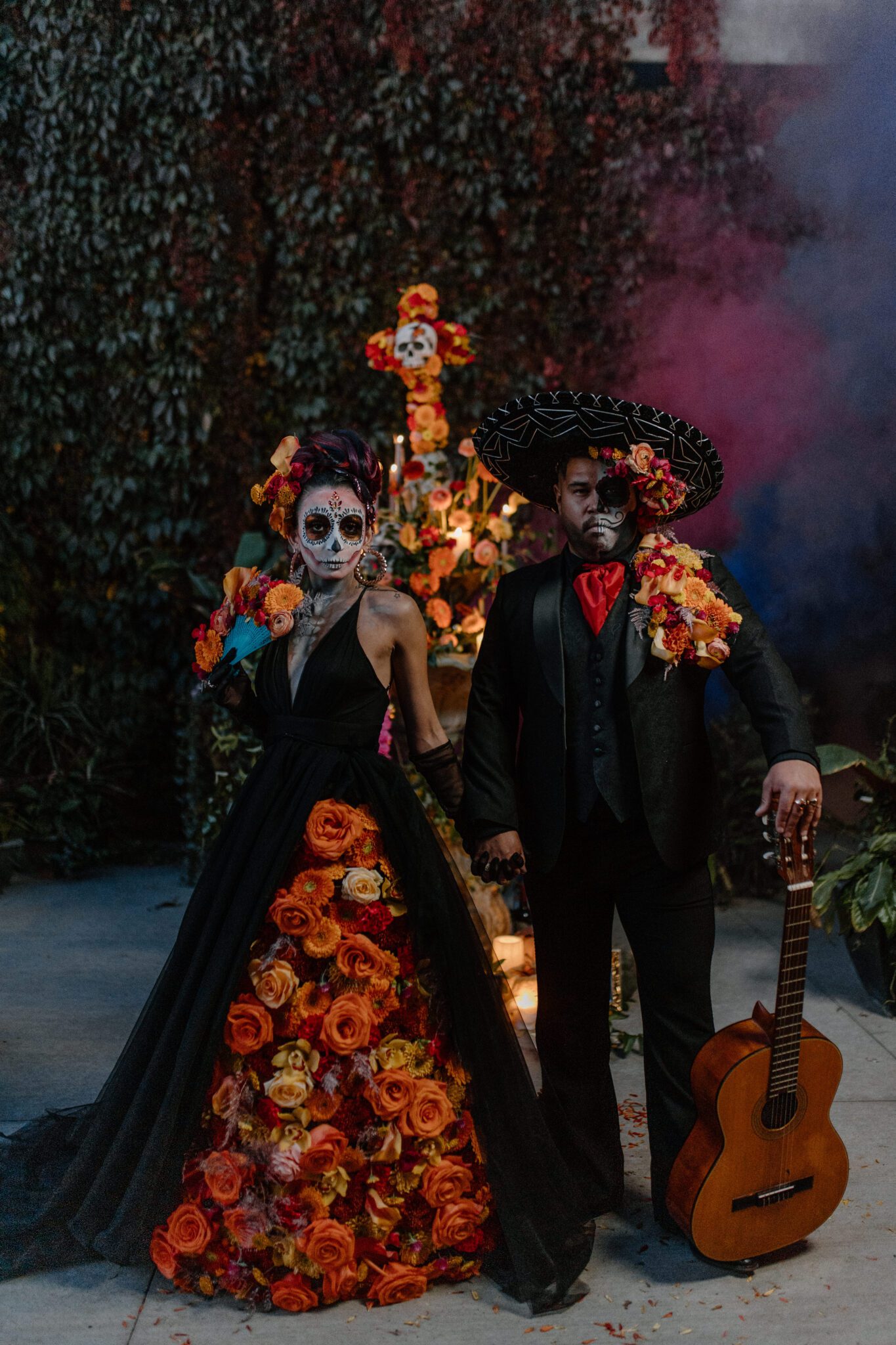 Day of the Dead couple holding hands, featuring black tulle dress and fiery fall florals by Calyx Floral Design. 