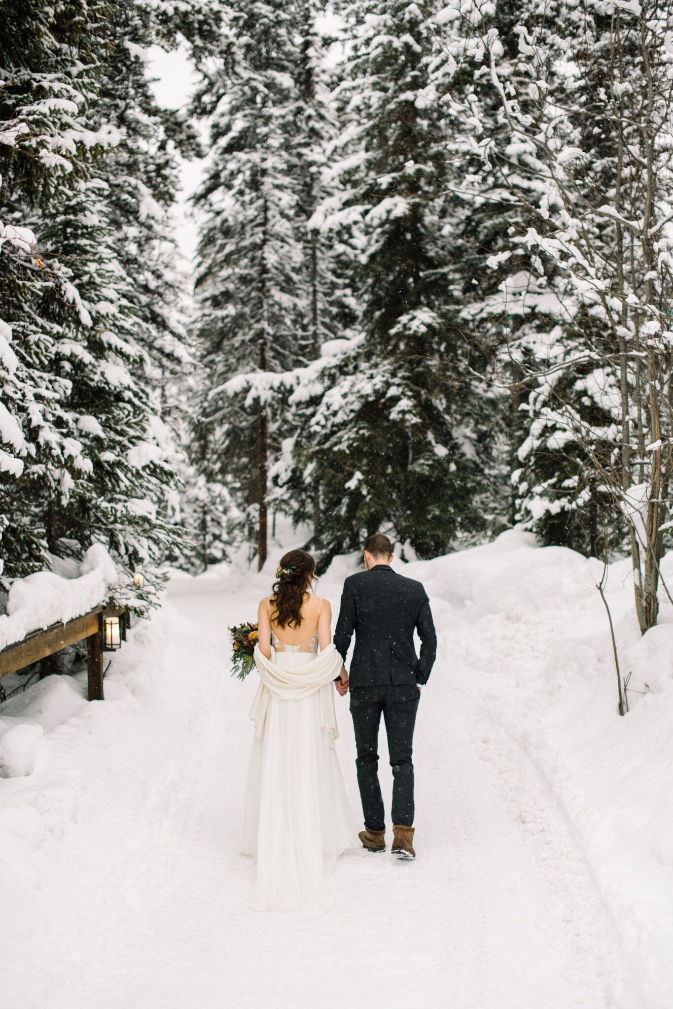 Portrait of couple walking in a snow-covered forest at Emerald Lake Lodge, winter wedding inspiration. 