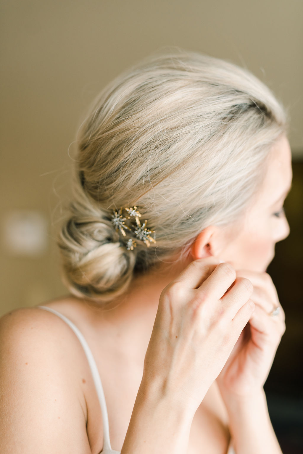 Bride getting ready for wedding day, putting on earrings, hair styled in an elegant updo, winter wedding inspiration. 