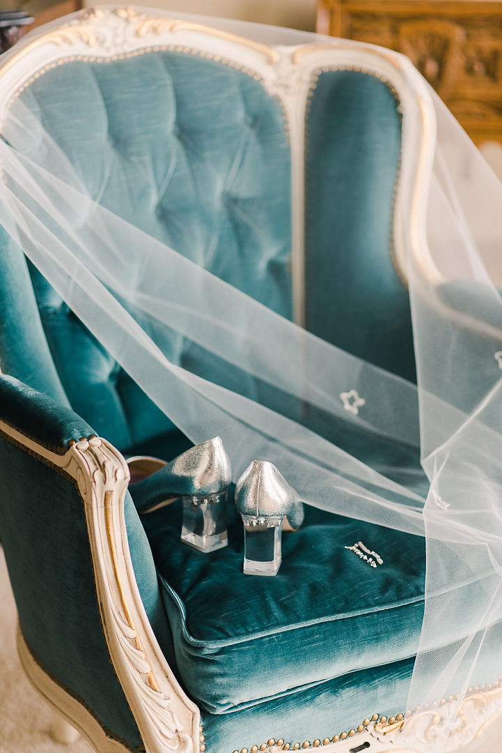 Portrait of getting ready details, elegant heels and veil over blue-coloured chair, winter wedding inspiration. 