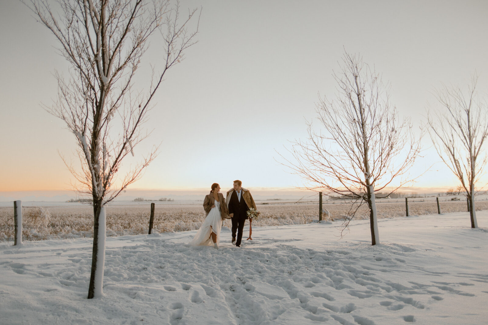 Portrait of bride and groom running through a snow covered field in Alberta, winter wedding inspiration. 