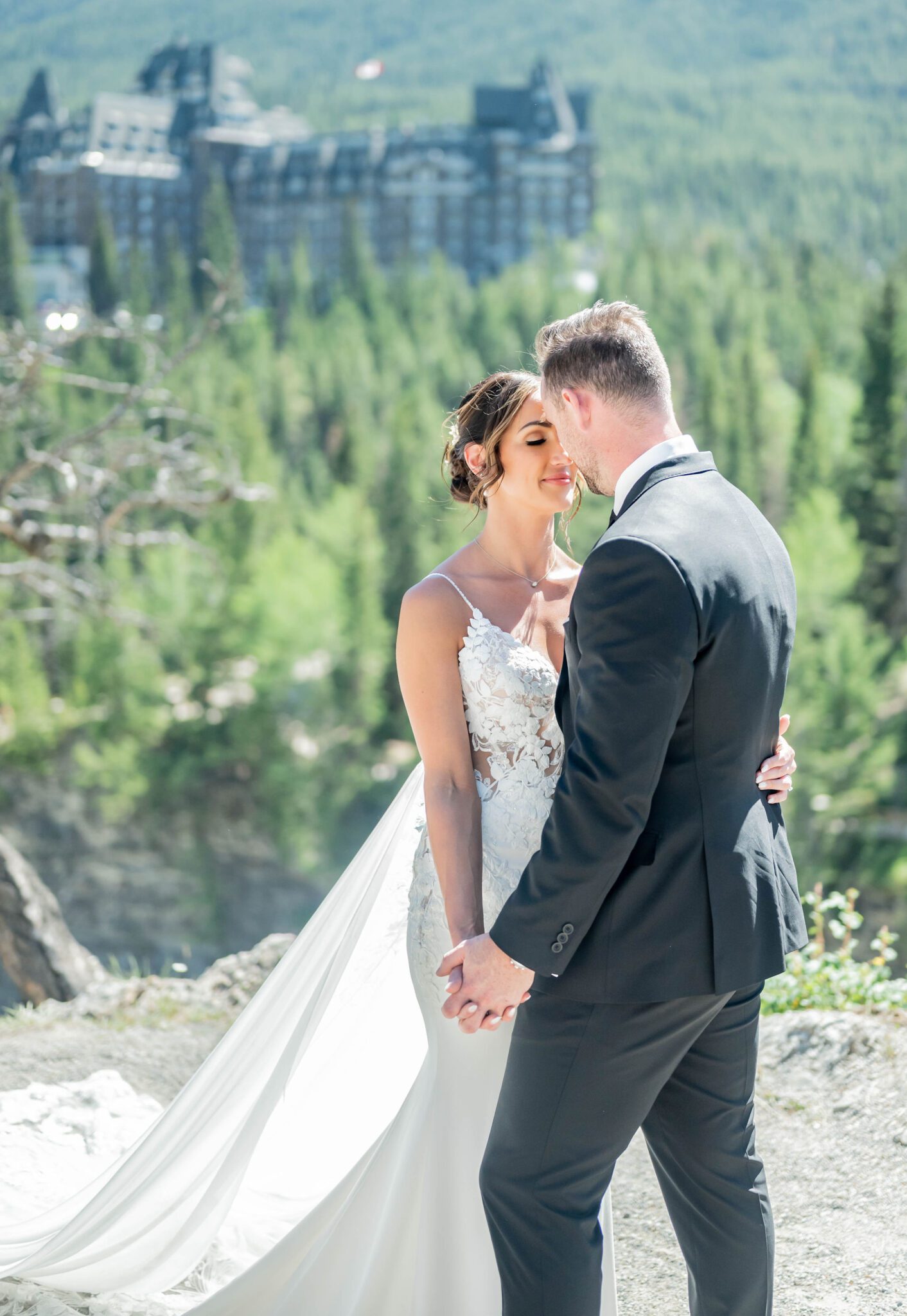 Bride and groom slow dancing in front of the Fairmont Banff Springs at their Banff Summer Wedding, bride in elegant lace gown, Alberta wedding inspiration. 