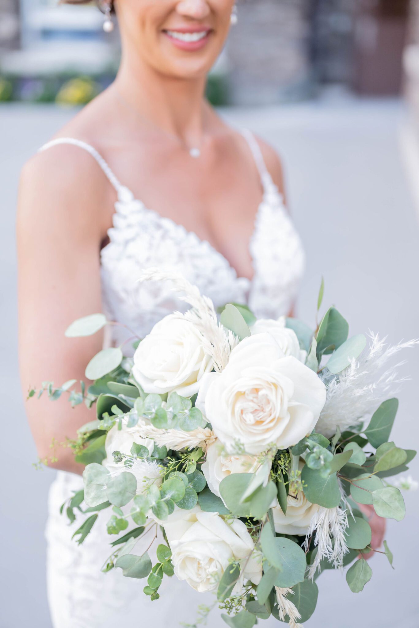 Bride in lace gown holding white floral bouquet with greenery, summer wedding inspiration. 