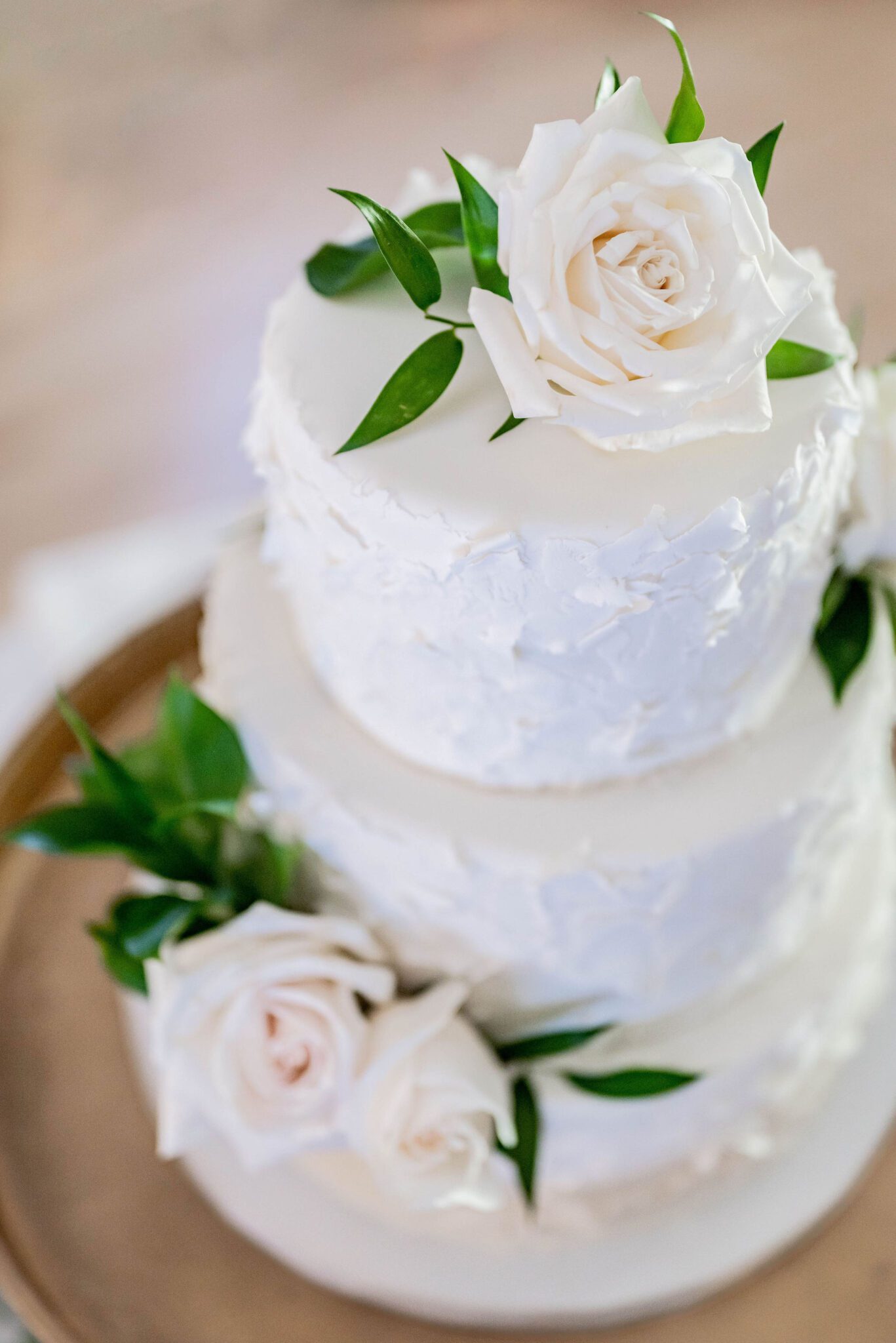 Elegant white wedding cake with added roses and greenery, classic wedding style inspiration. 