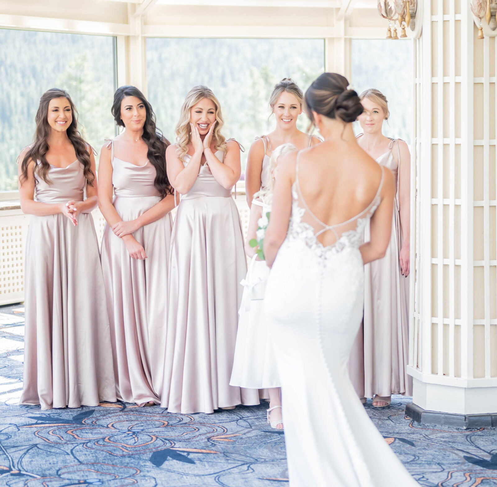 Bridesmaid first look reaction to the bride in elegant lace gown at the Fairmont Banff Springs. Floor length champagne coloured bridesmaid dress inspiration