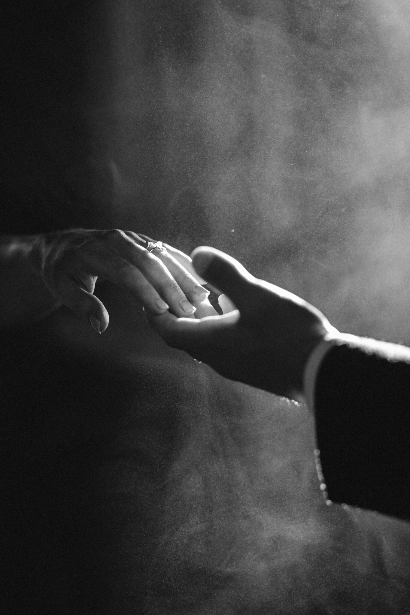 Black and white portrait of bride and groom lightly touching hands, hazy sun-kissed atmosphere, film photography style. 