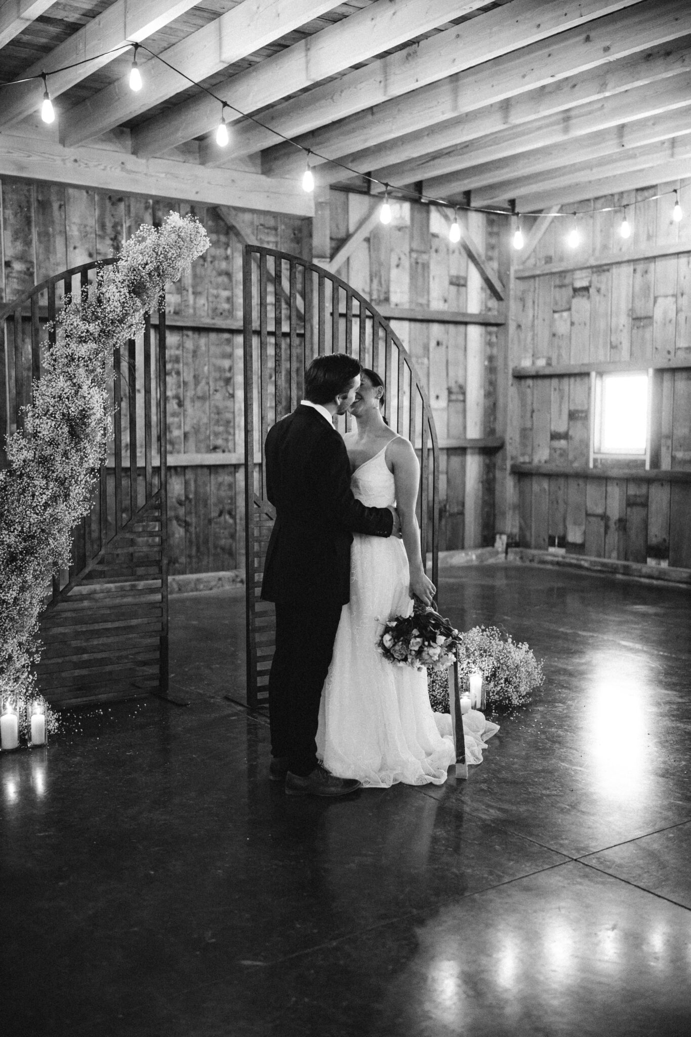 Modernized and updated take on a baby's breath installation for the ceremony arch at this Country Chic style wedding inspiration at Countryside Barn in Lethbridge Alberta, Celebratory first kiss at wedding ceremony, modern country wedding style, bride and groom kiss front of the ceremony arch