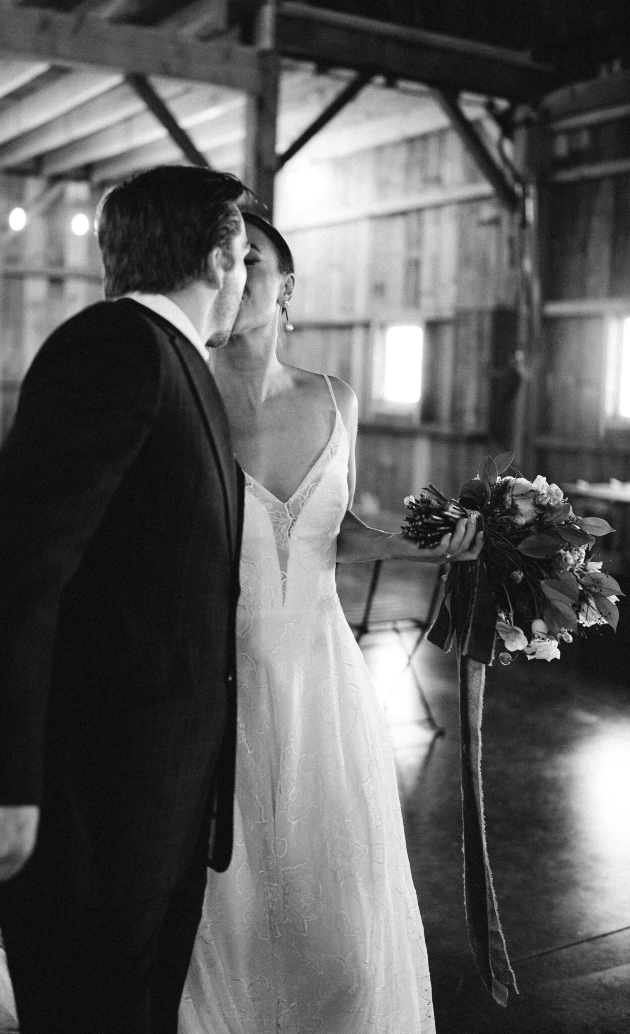 Bride and groom share a kiss at the end of the wedding ceremony aisle, bride holding wedding bouquet, black and white photography. 
