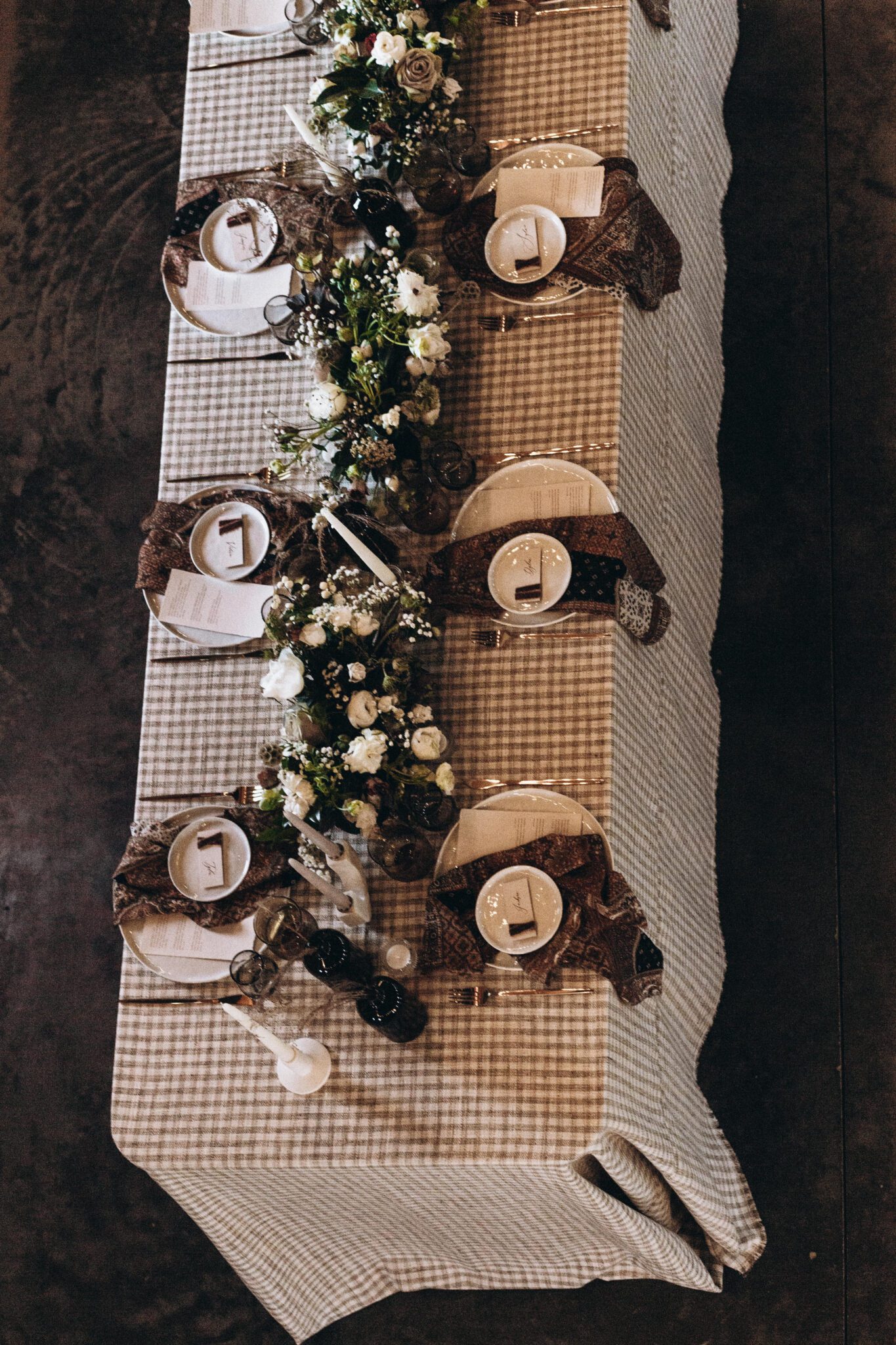 Country Chic style wedding inspiration with patterned tablescape, checkered and textured linens, unique and earthy florals covering the table, flatlay style photo. 
