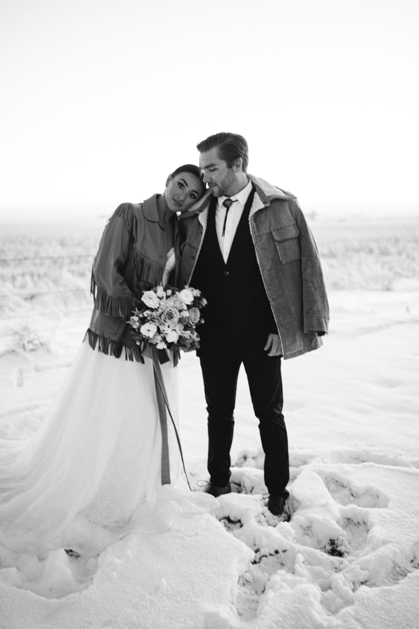 Contemporary meets vintage in this country chic wedding inspiration in Alberta, featuring the bride and groom kissing for wedding portraits outside in the snow, winter wedding portrait ideas, winter wedding inspiration, groom's vintage bolo tie and thrifted suede fringe jacket from Alice & Irene. 