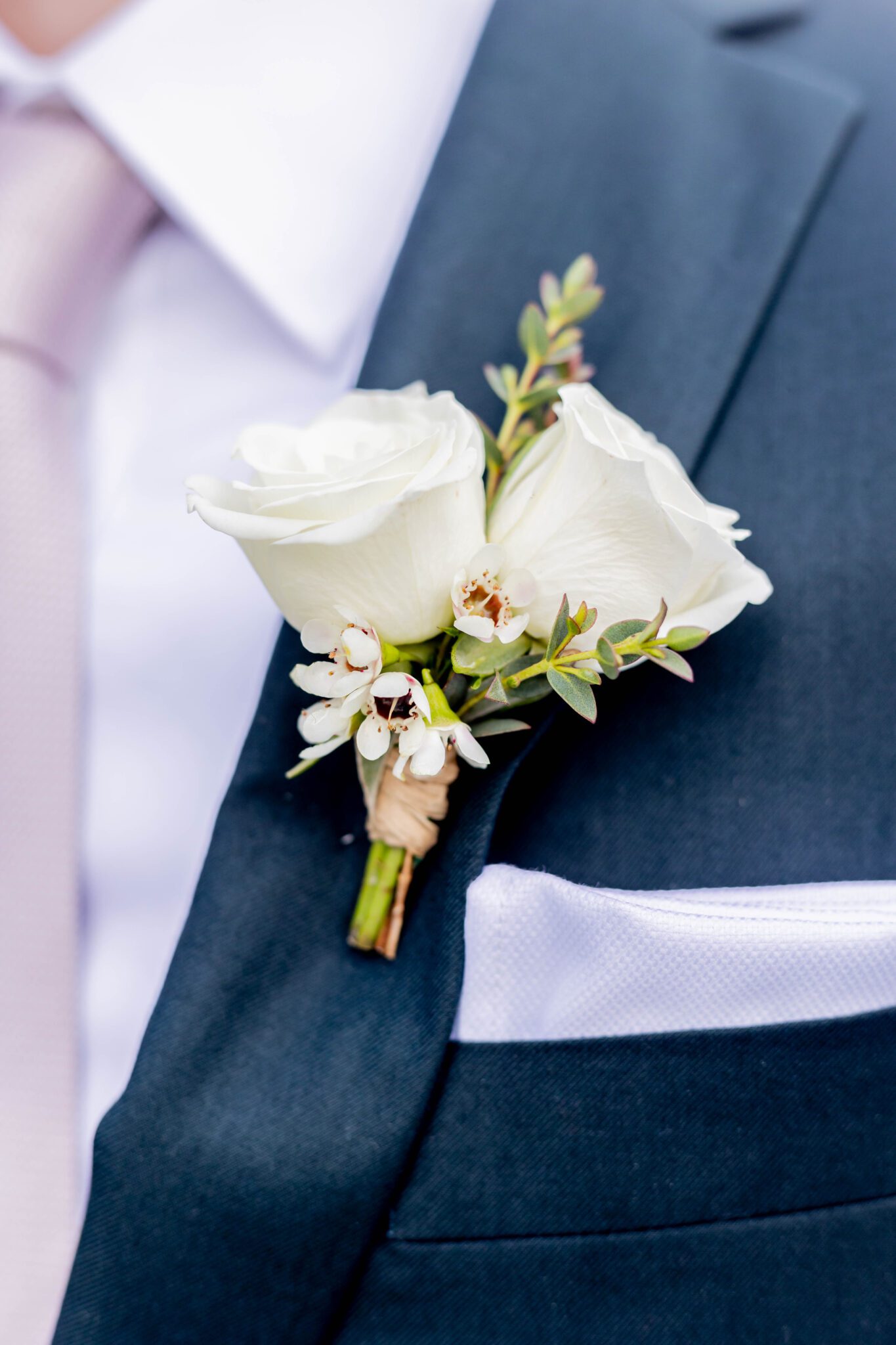 Close up portrait of groom's boutonnière complimented by navy blue suite and light pink tie. 