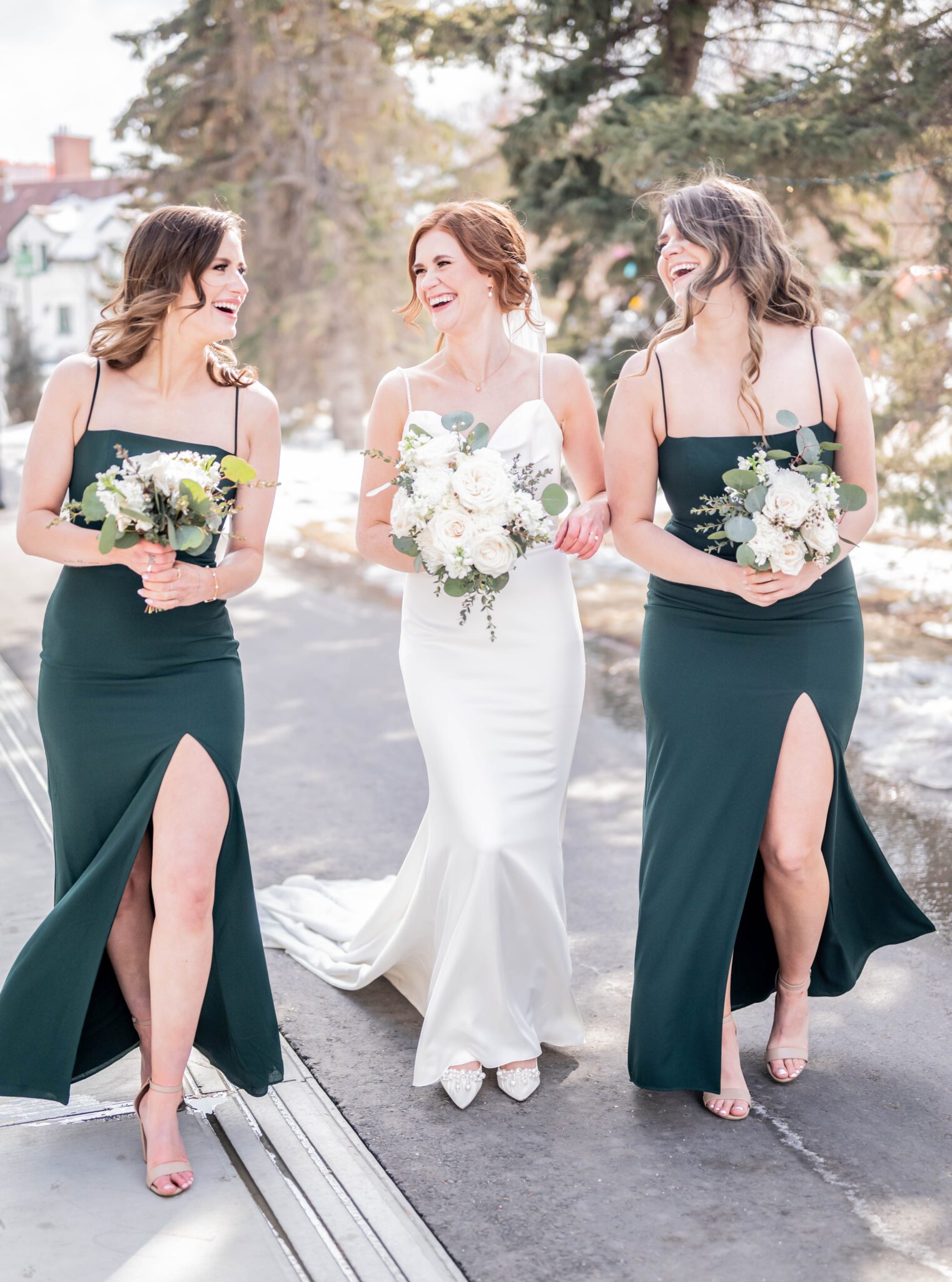 Bride and bridesmaids walk down path near the wedding venue, holding classic white floral bouquets. Bridesmaids are seen wearing emerald coloured gowns from Park and Fifth, bridesmaid photo inspiration.